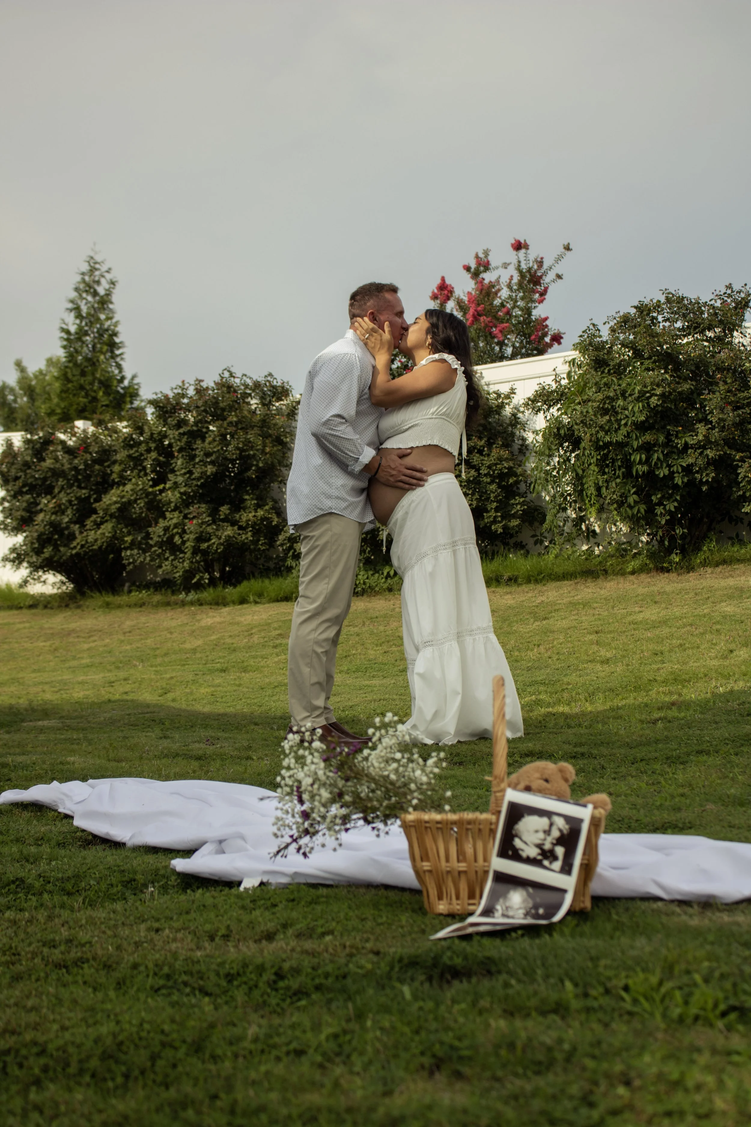 A couple kissing during an outdoor wedding ceremony on a grassy lawn with decorated setup, flowers, and a teddy bear.