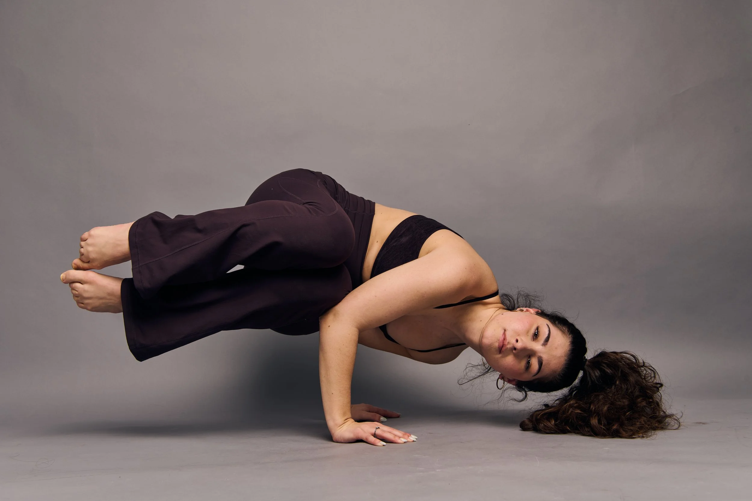 A woman practicing yoga in a plank pose against a plain gray background.
