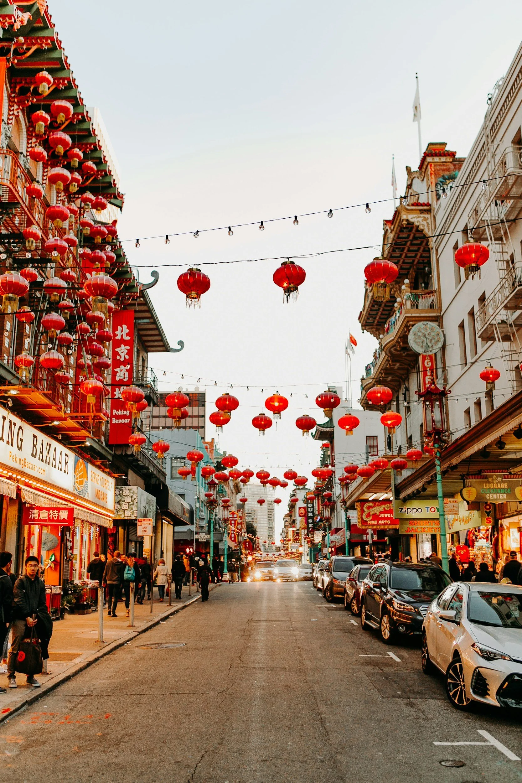 Red lanterns hanging above a street in San Francisco’s Chinatown, lined with neighborhood shops and buildings.