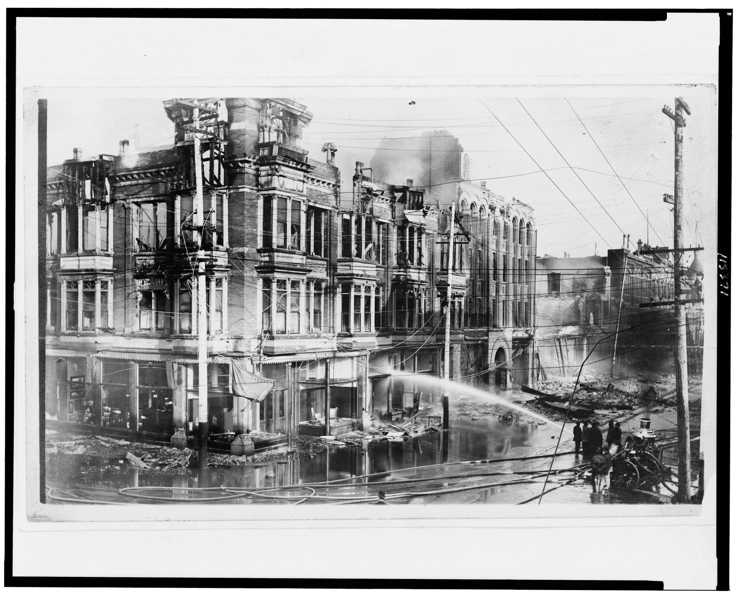 Black-and-white photograph of firefighters spraying water across damaged buildings and debris after the 1906 San Francisco earthquake.