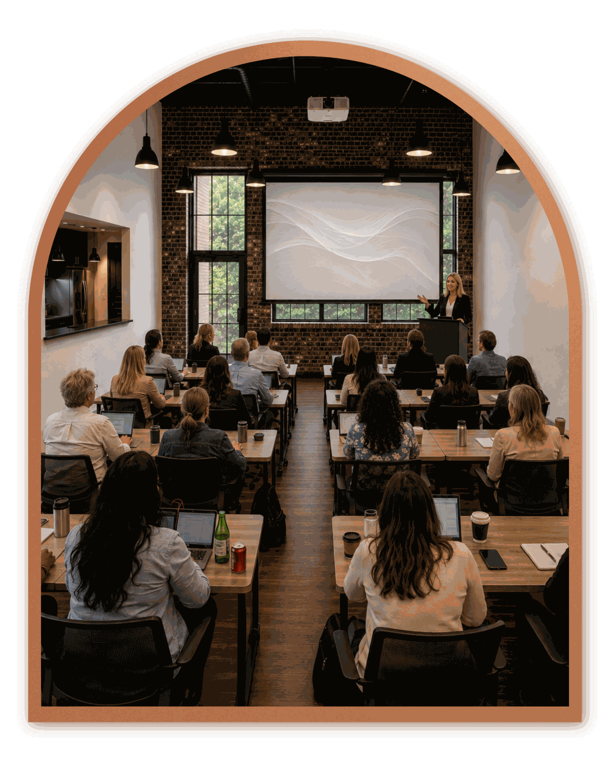 People at tables with laptops facing a presenter in a brick-walled room