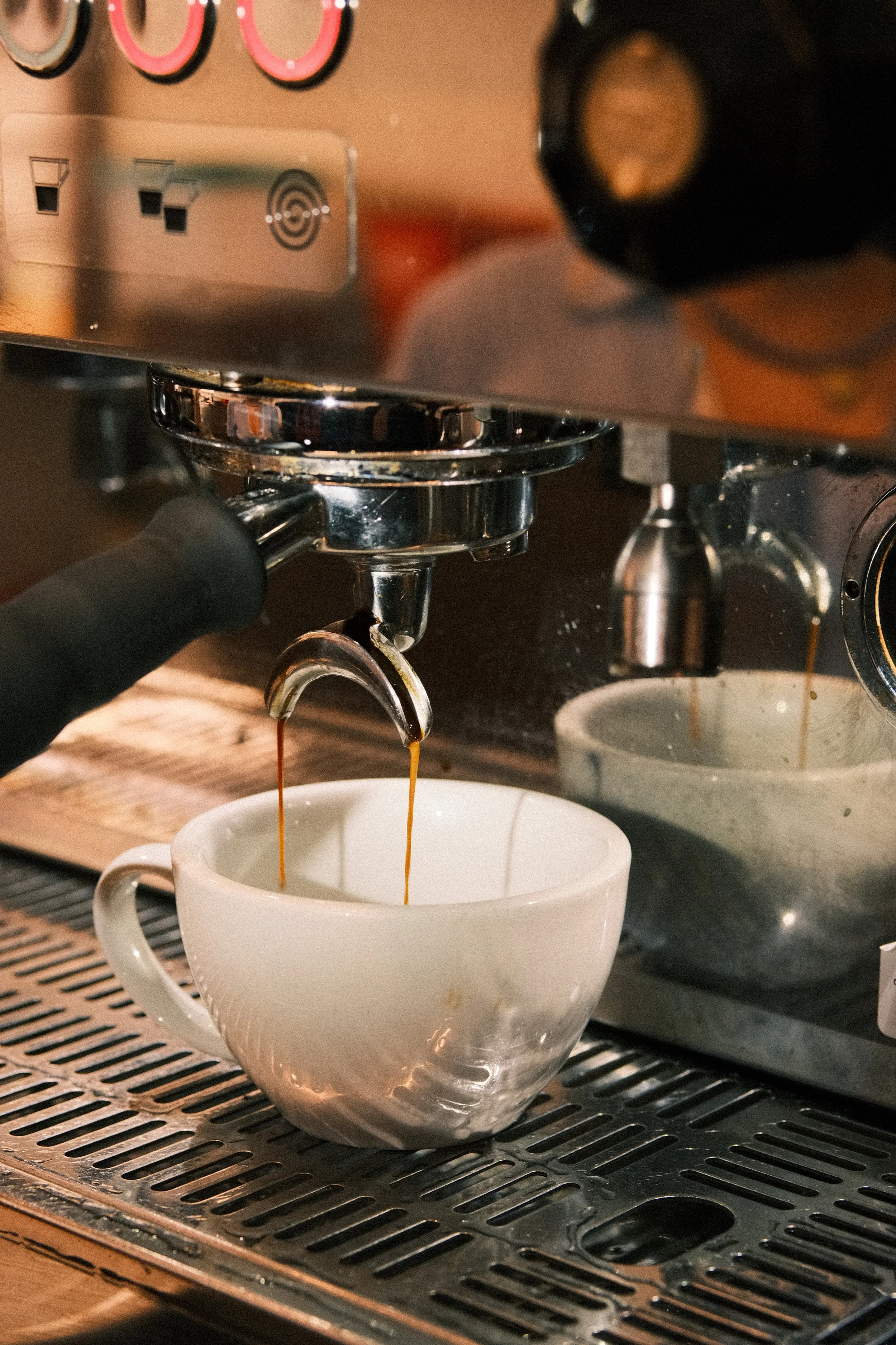 Close-up of an espresso machine pouring espresso into a white ceramic cup on a drip tray.