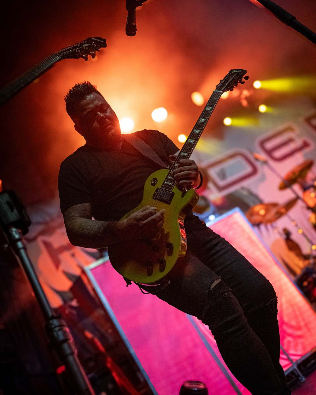 A musician playing an electric guitar on stage with colorful lights in the background and a large screen displaying visuals.