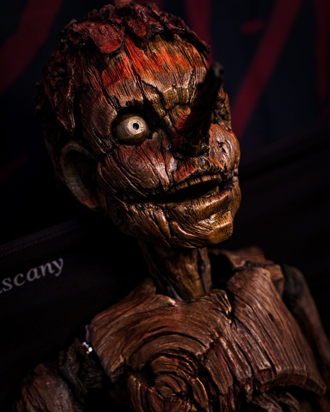 A detailed wooden sculpture of a smiling, animated face with one large, round eye and a slightly tilted head.
