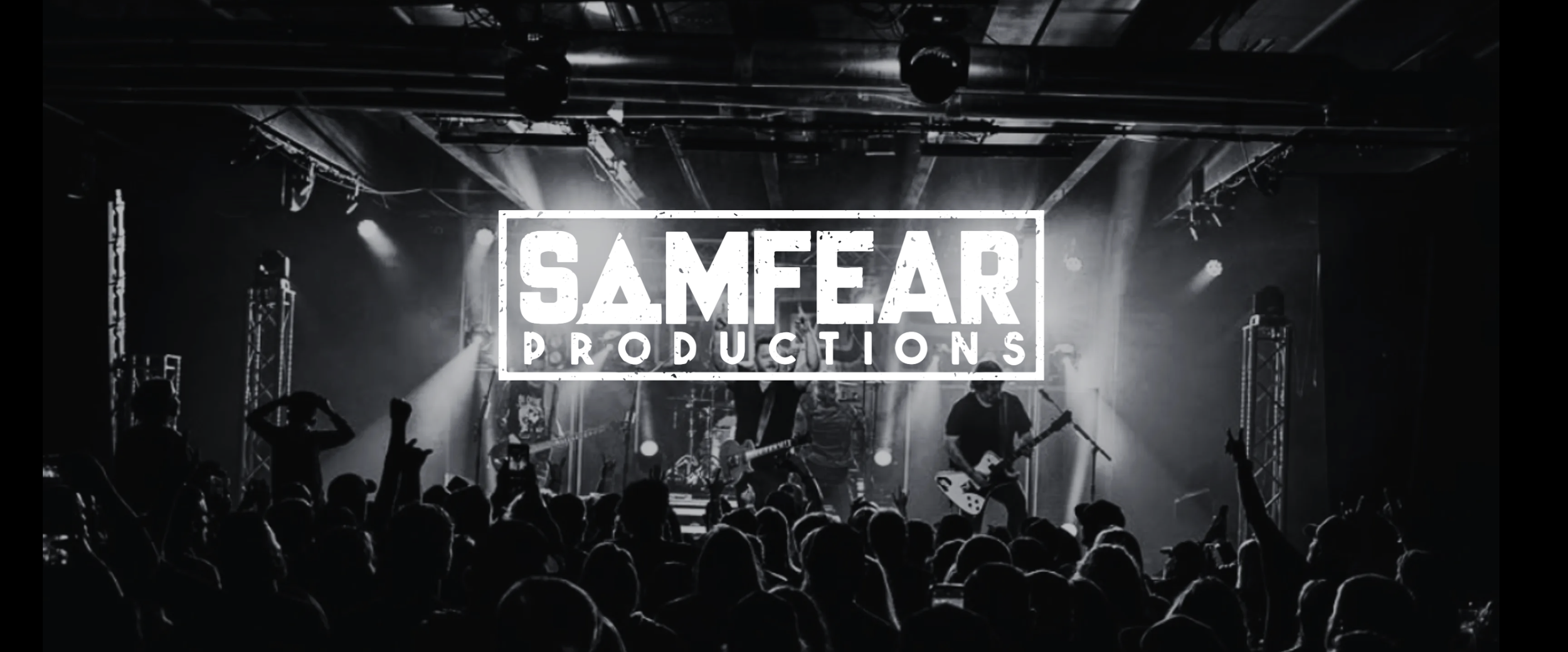 A black and white photo of a live concert with a band on stage, audience members with raised hands, and a prominent logo saying 'SAMEFARI PRODUCTIONS' in the center.