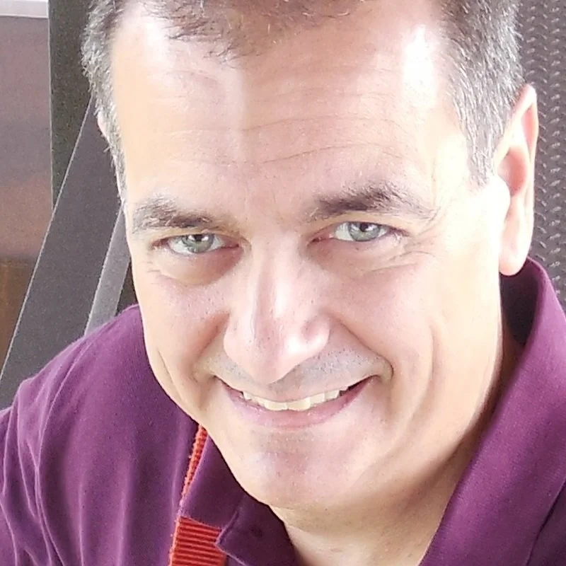 A smiling man with short hair, wearing a dark purple shirt, looking at the camera.