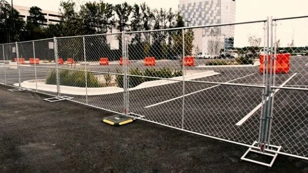 Empty parking lot surrounded by temporary chain-link fencing with orange barriers in the background.
