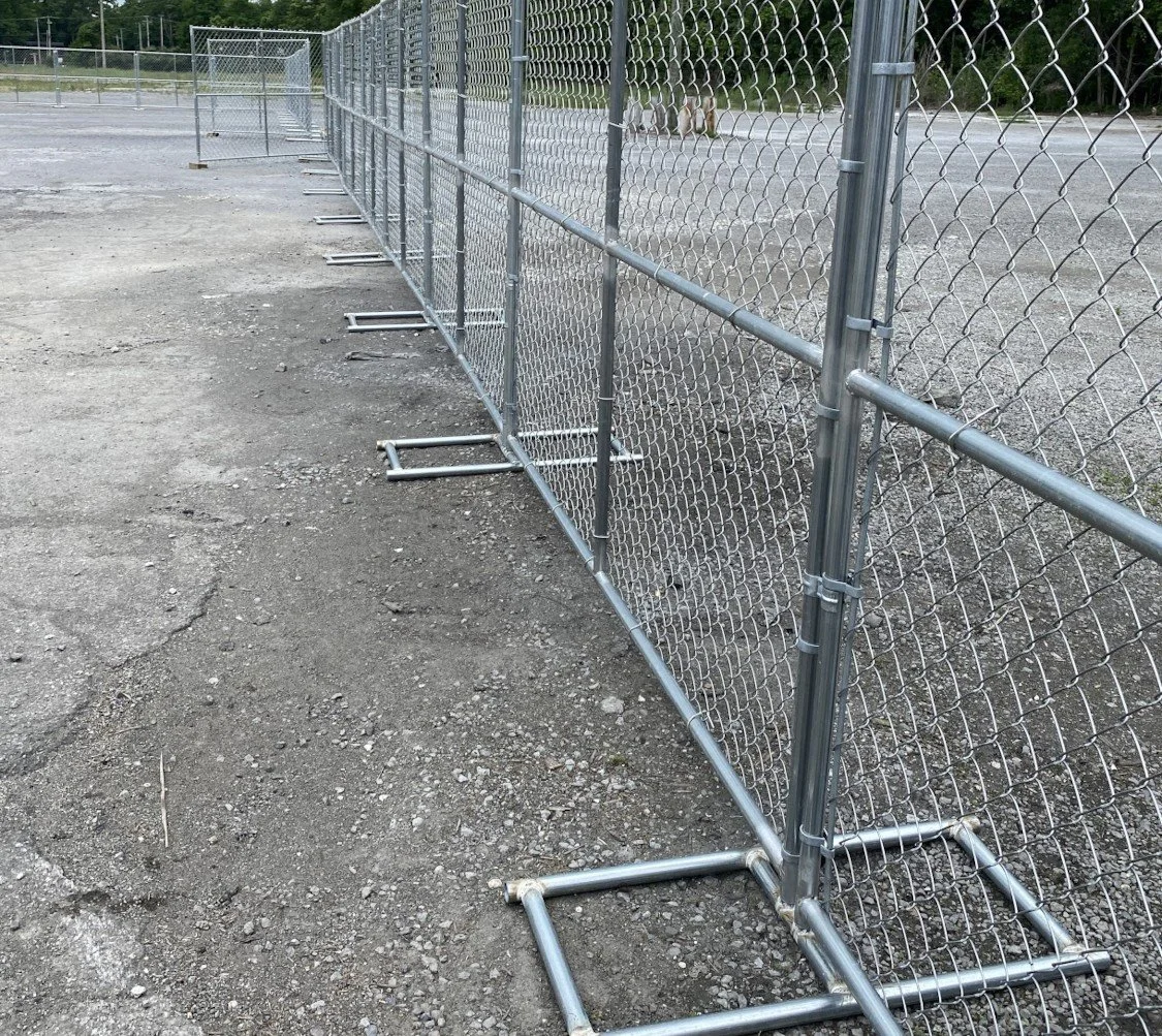 Metal chain-link fence panels on a gravel outdoor surface, with two dogs in the background.