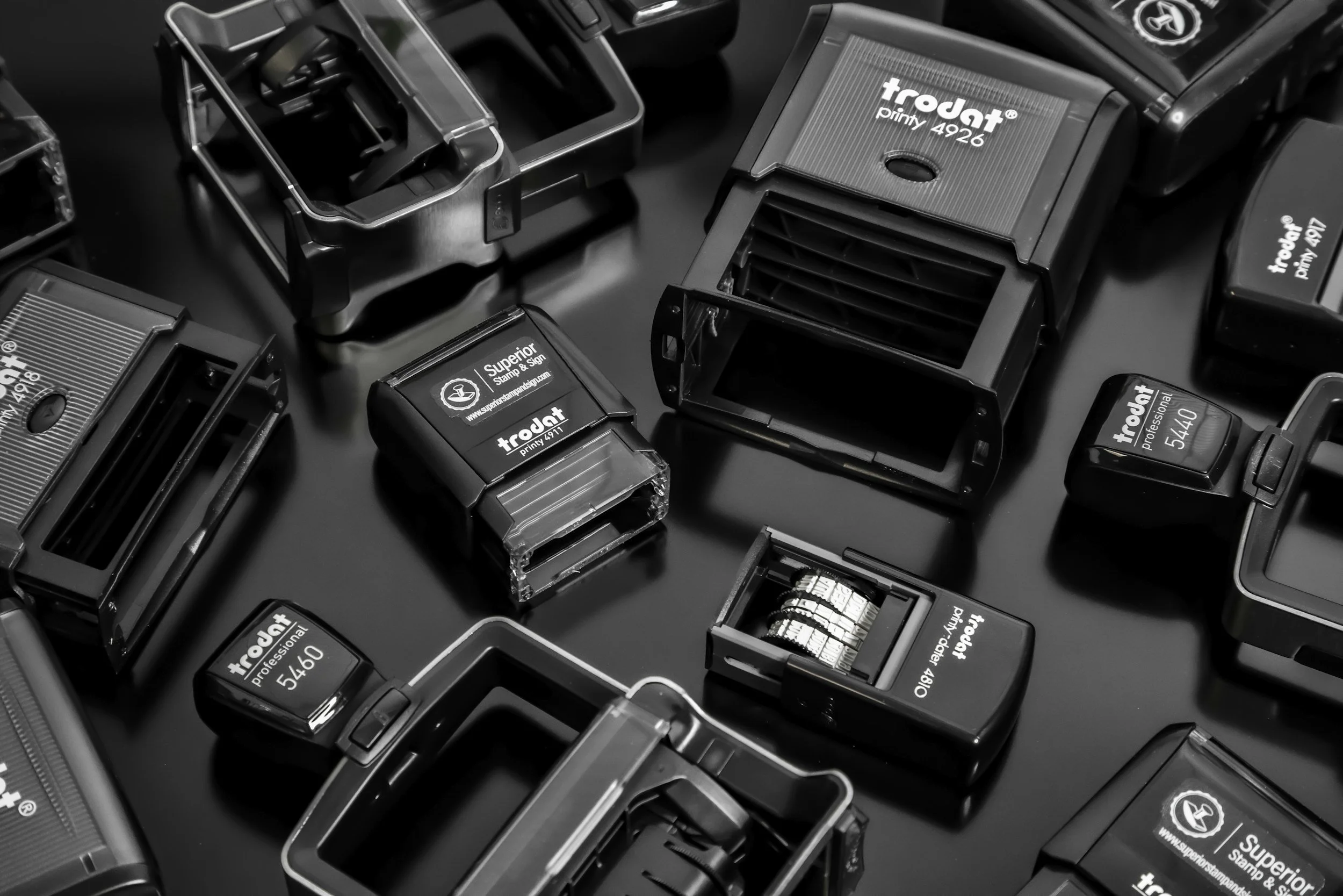 Black and white photograph of multiple rubber stamps with various designs and text on their surfaces, arranged randomly on a dark surface.