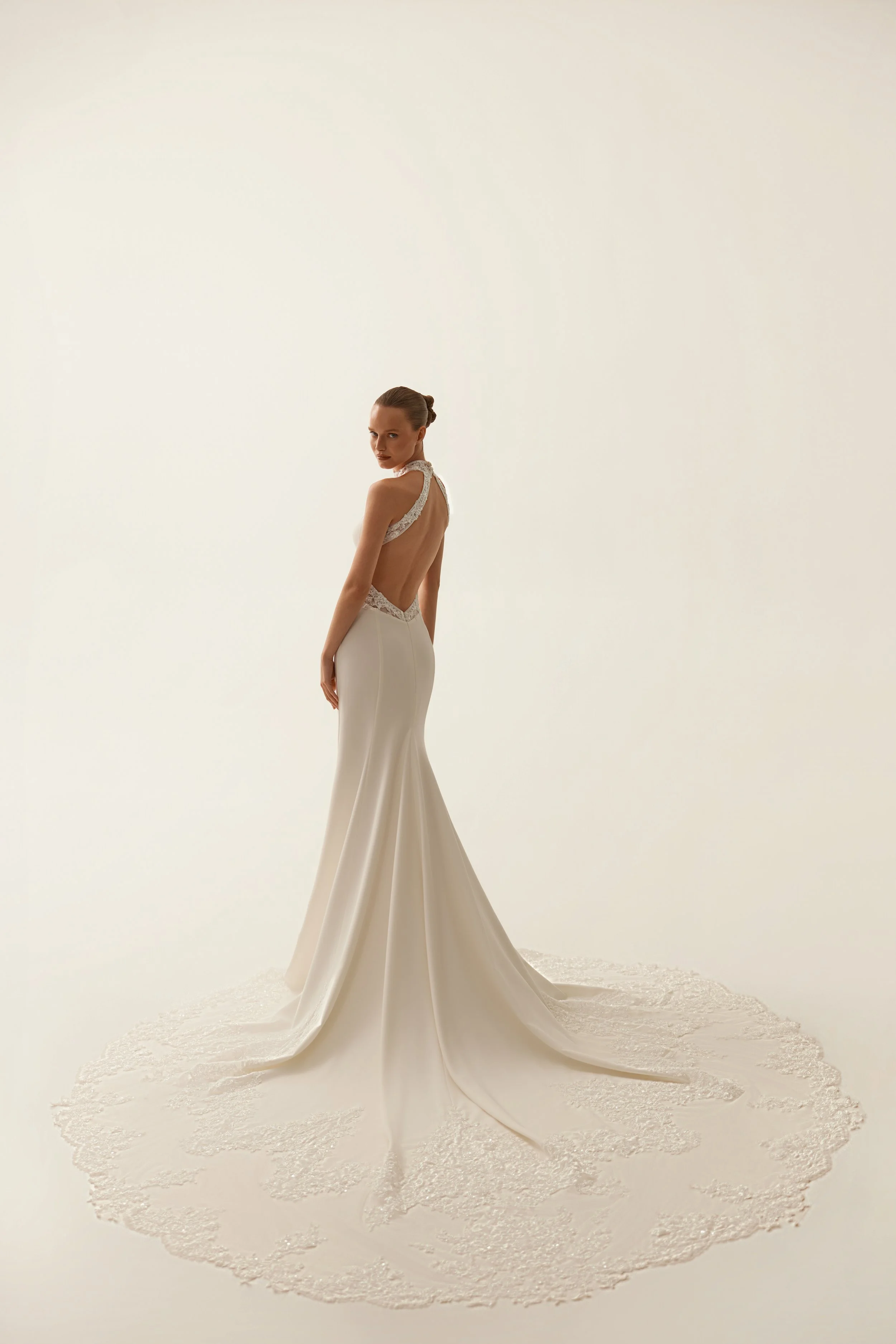 Bride modeling a white high necked wedding gown by Maison Yana with an open back and sweeping train