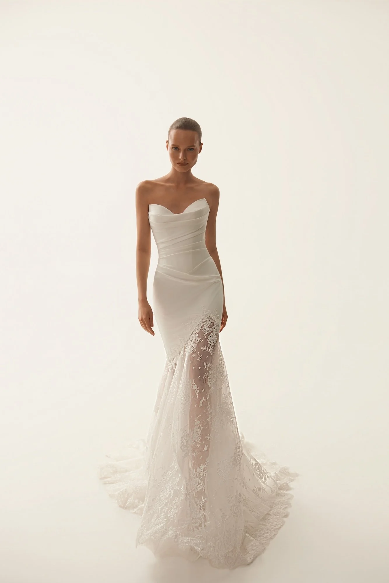 Model wearing an ivory strapless mermaid wedding gown by Maison Yana with draped fabric and floral lace train