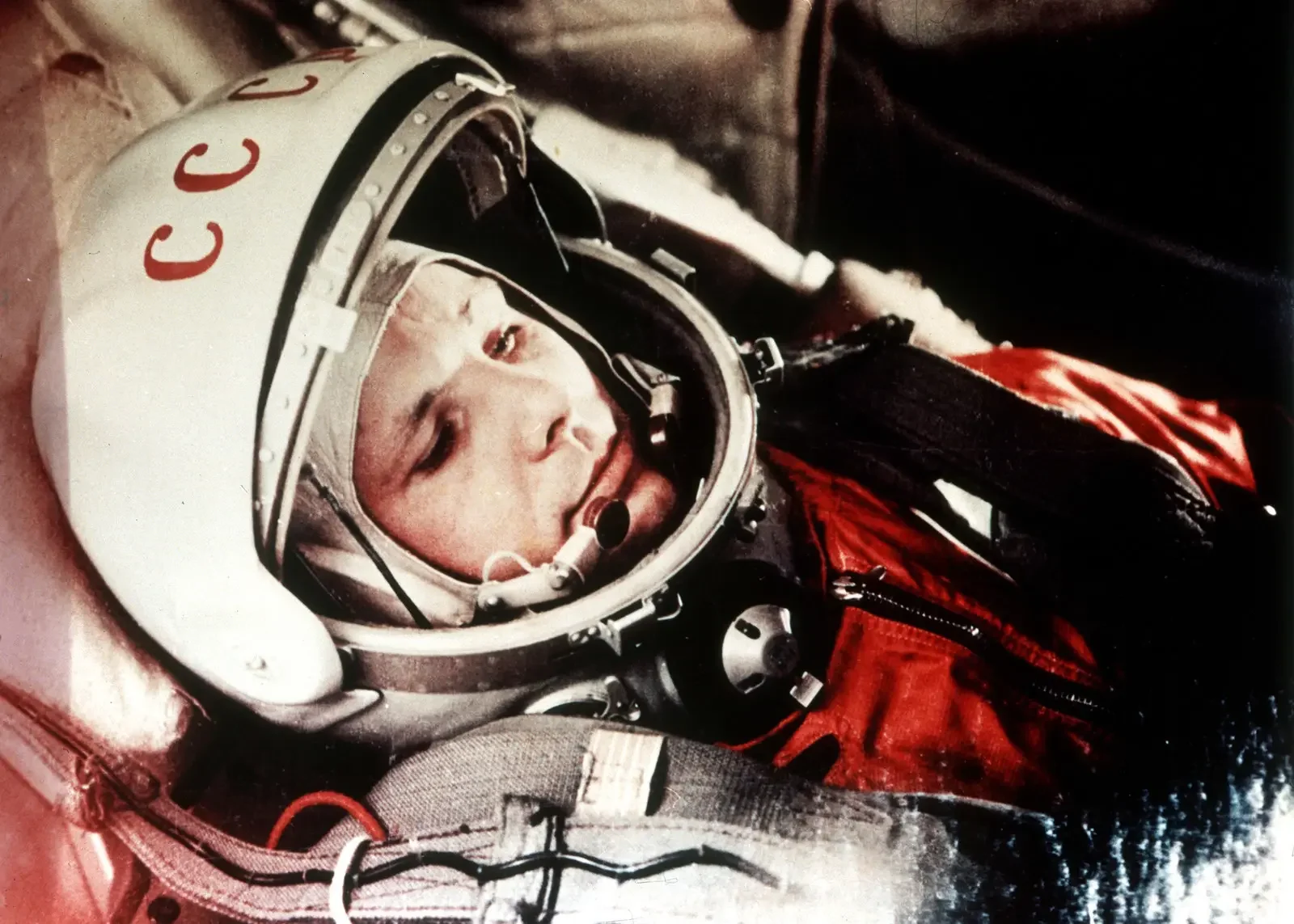 Close-up of a young astronaut wearing a helmet with the NASA logo and a red flight suit, seated inside a spacecraft.