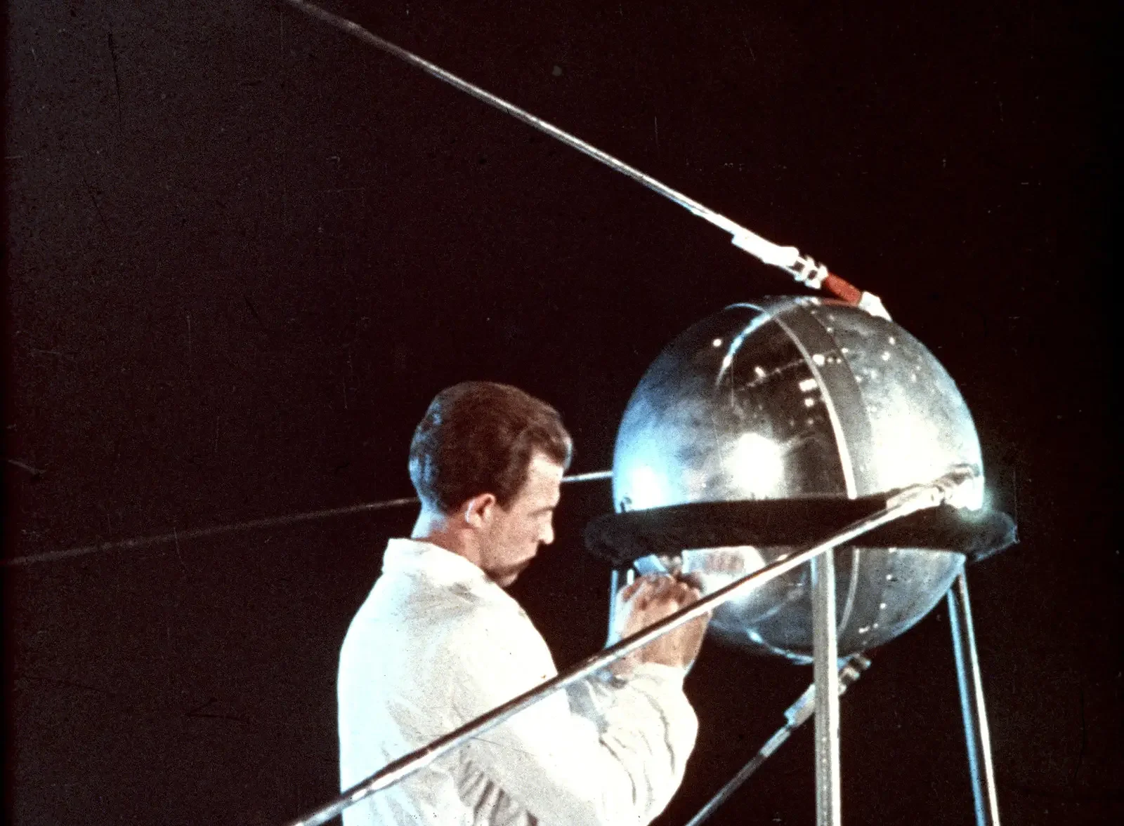 A man working with a large, reflective spherical object in a dark environment, possibly a laboratory or scientific setting.