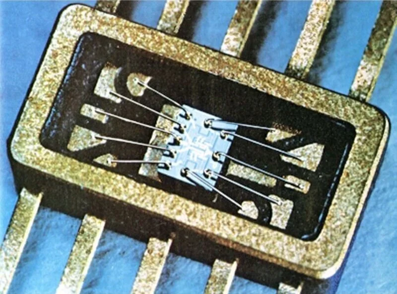 Close-up of a vintage electronic component with gold-colored pins and a black rectangular base, mounted on a blue surface with parallel gold connectors.