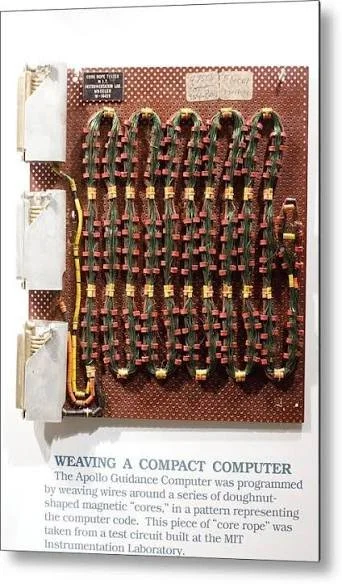 A display of woven magnetic cores shaped like doughnuts, arranged in five rows on a red background, with a piece of printed informational text about building a compact computer from magnetic cores.