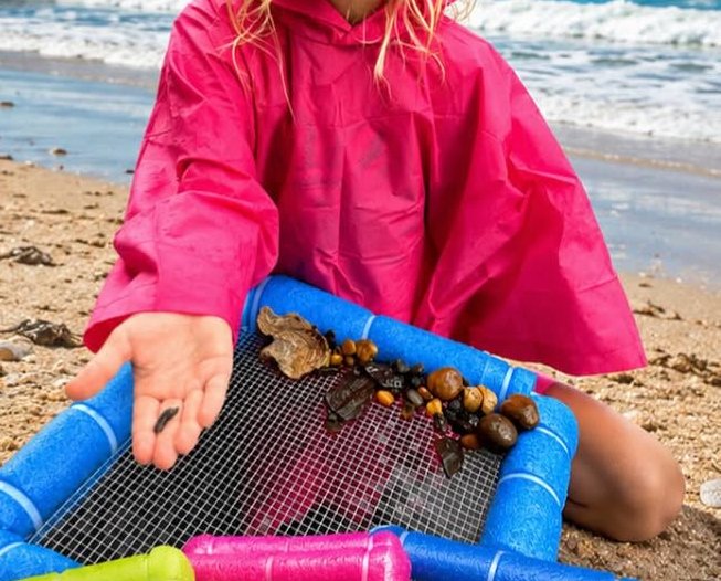 Child on the beach wearing a pink raincoat and holding a shark tooth found with Isla's shore sifters