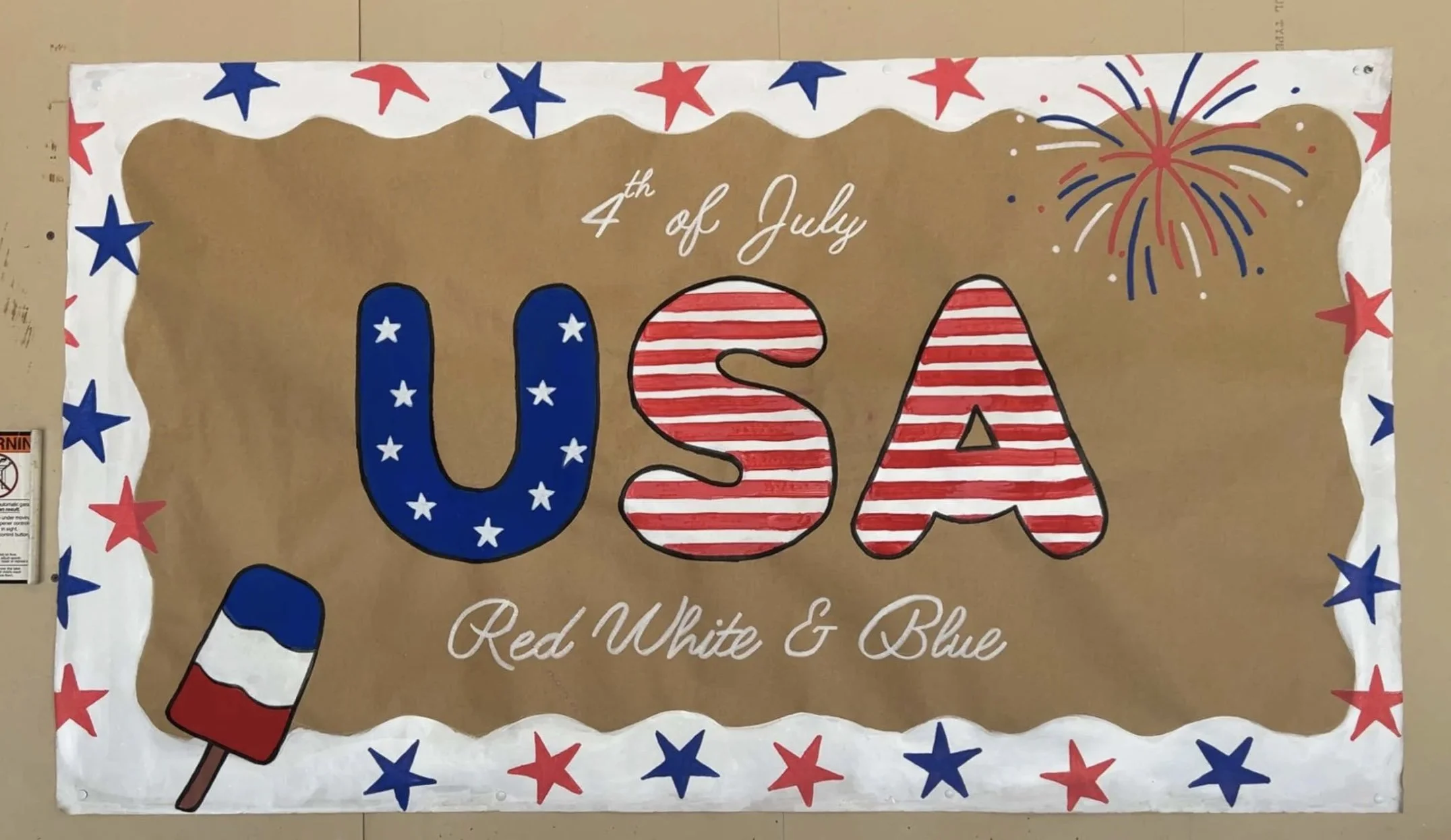 Patriotic 4th of July banner with large letters spelling 'USA' decorated with American flag patterns, surrounded by red, white, and blue stars, a firework graphic, and a red white and blue popsicle.
