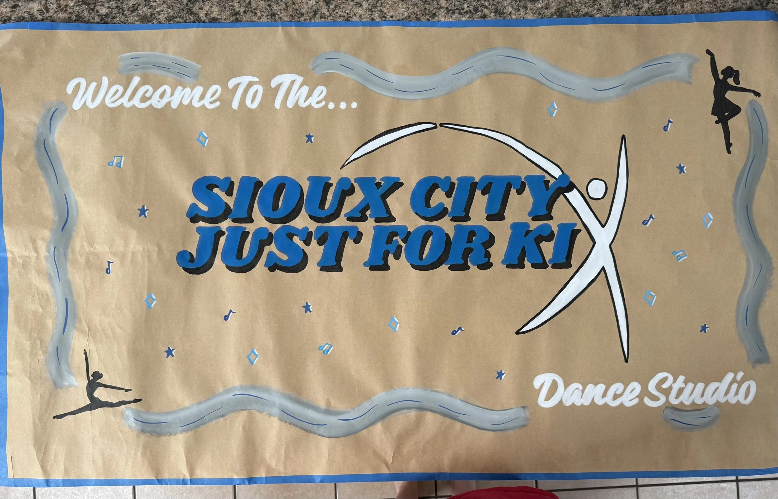 Decorative poster welcoming visitors to Sioux City Just For Kix dance studio, with images of a dancer and a ballet dancer, music notes, and a wavy border.
