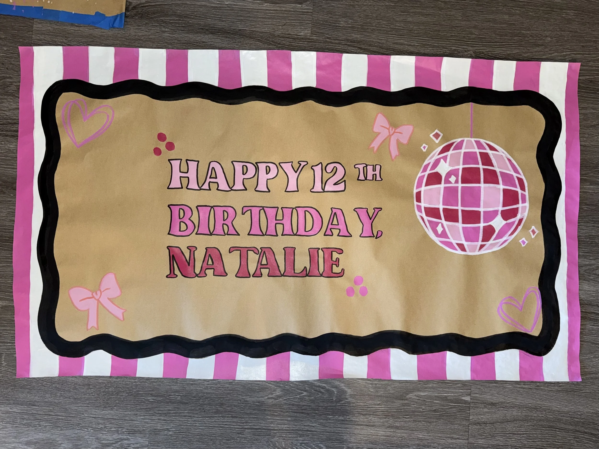 A colorful birthday banner with the message 'Happy 12th Birthday, Natalie' written in pink letters. The banner has a pink and white striped border, a pink disco ball on the right, pink hearts, and bows as decorations.