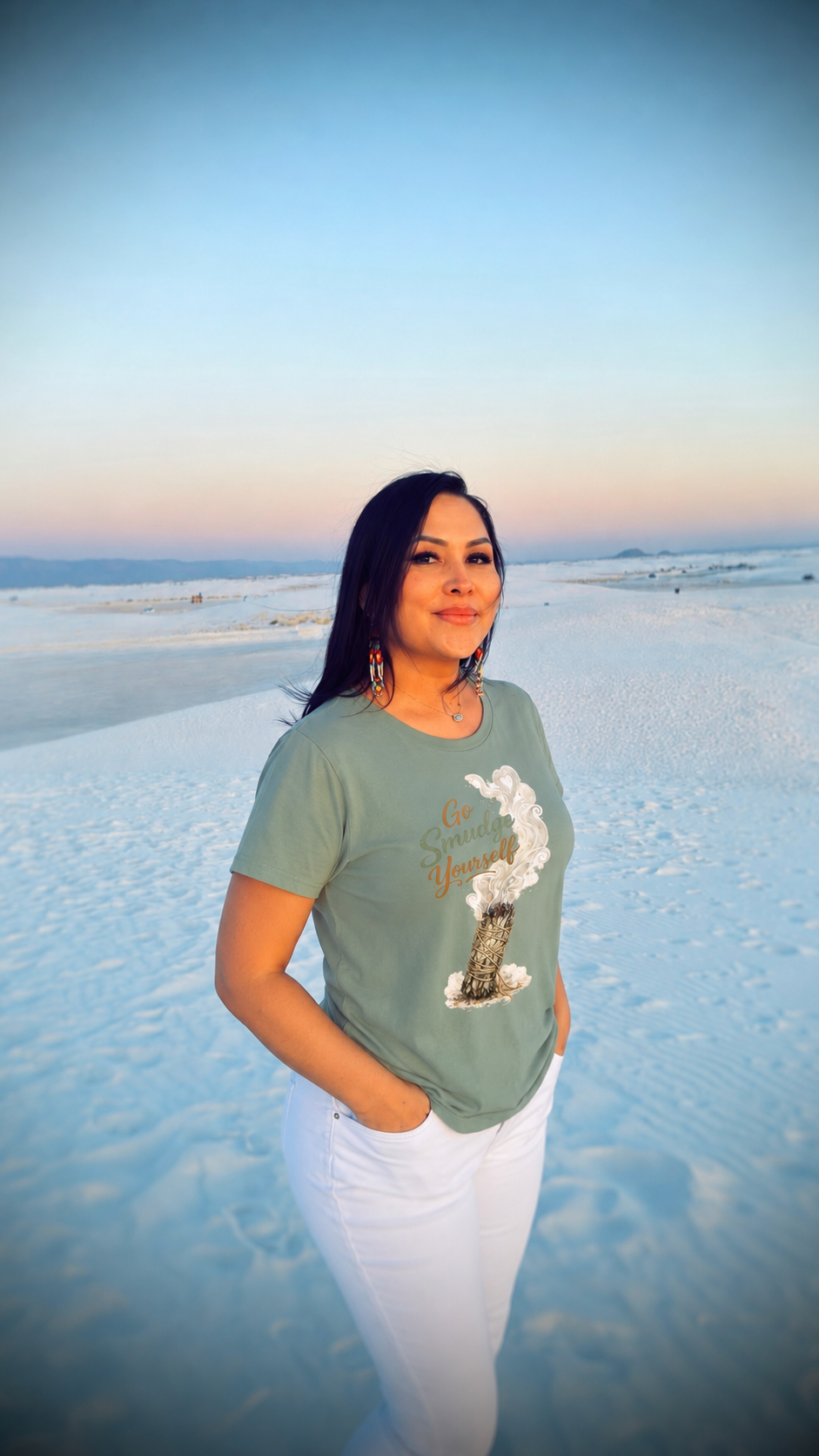 Woman standing on a white salt flat during sunset, wearing a green t-shirt and white pants.