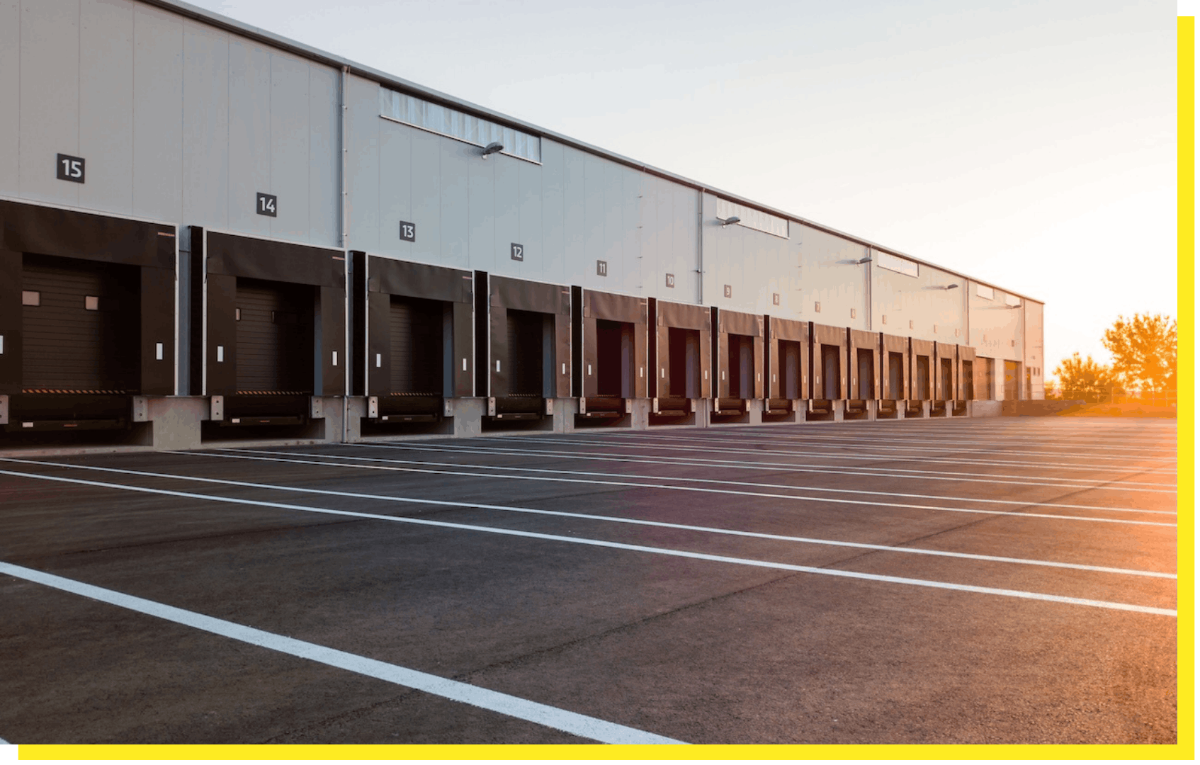 Large warehouse with multiple loading docks and empty parking spaces at sunrise or sunset.