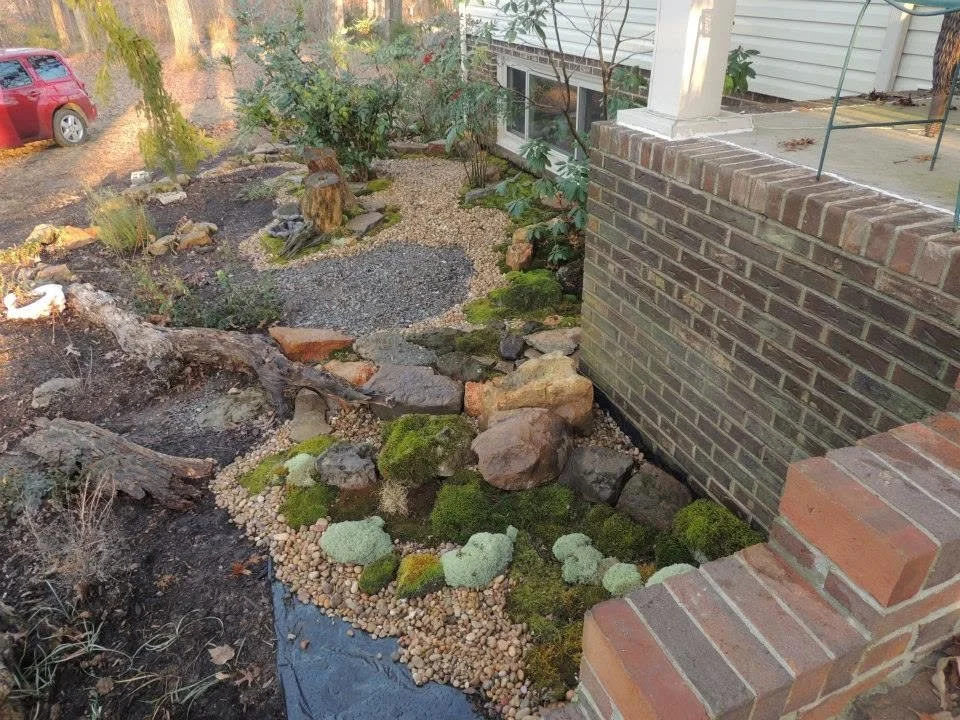 A landscaped front yard with rocks, moss, and gravel