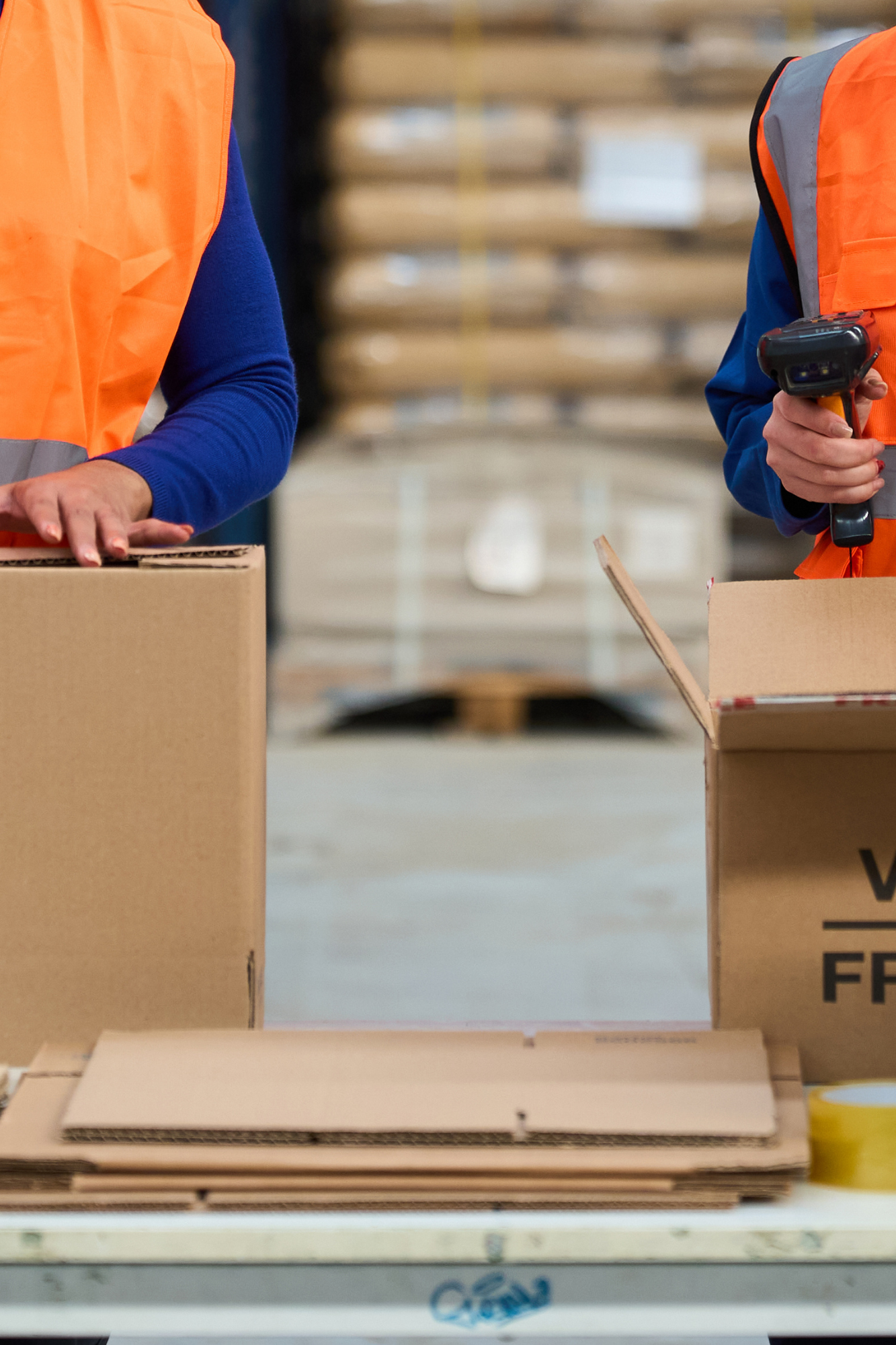 People in safety vests packing boxes in a warehouse.