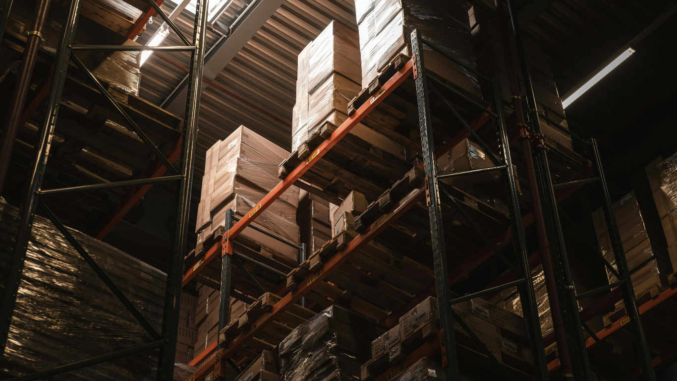 Warehouse storage with tall shelving units filled with boxes and pallets of goods.