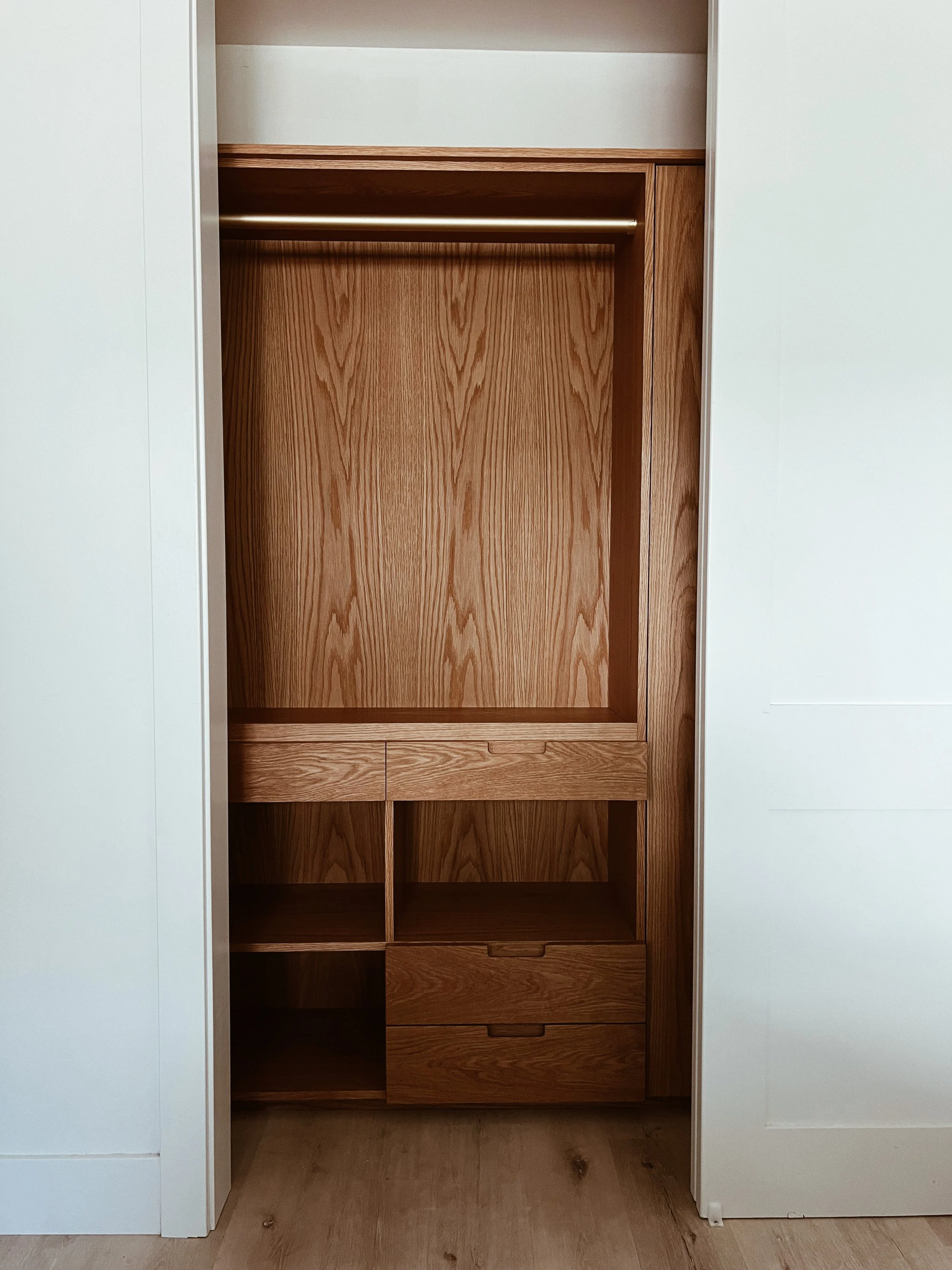 Open built-in wooden closet or cabinet with shelves and drawers, surrounded by white walls.