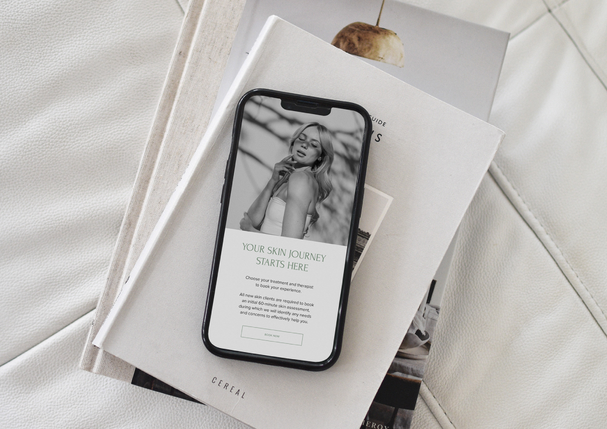 Smartphone displaying a skin care app with a photo of a woman, placed on magazines and a white leather surface.