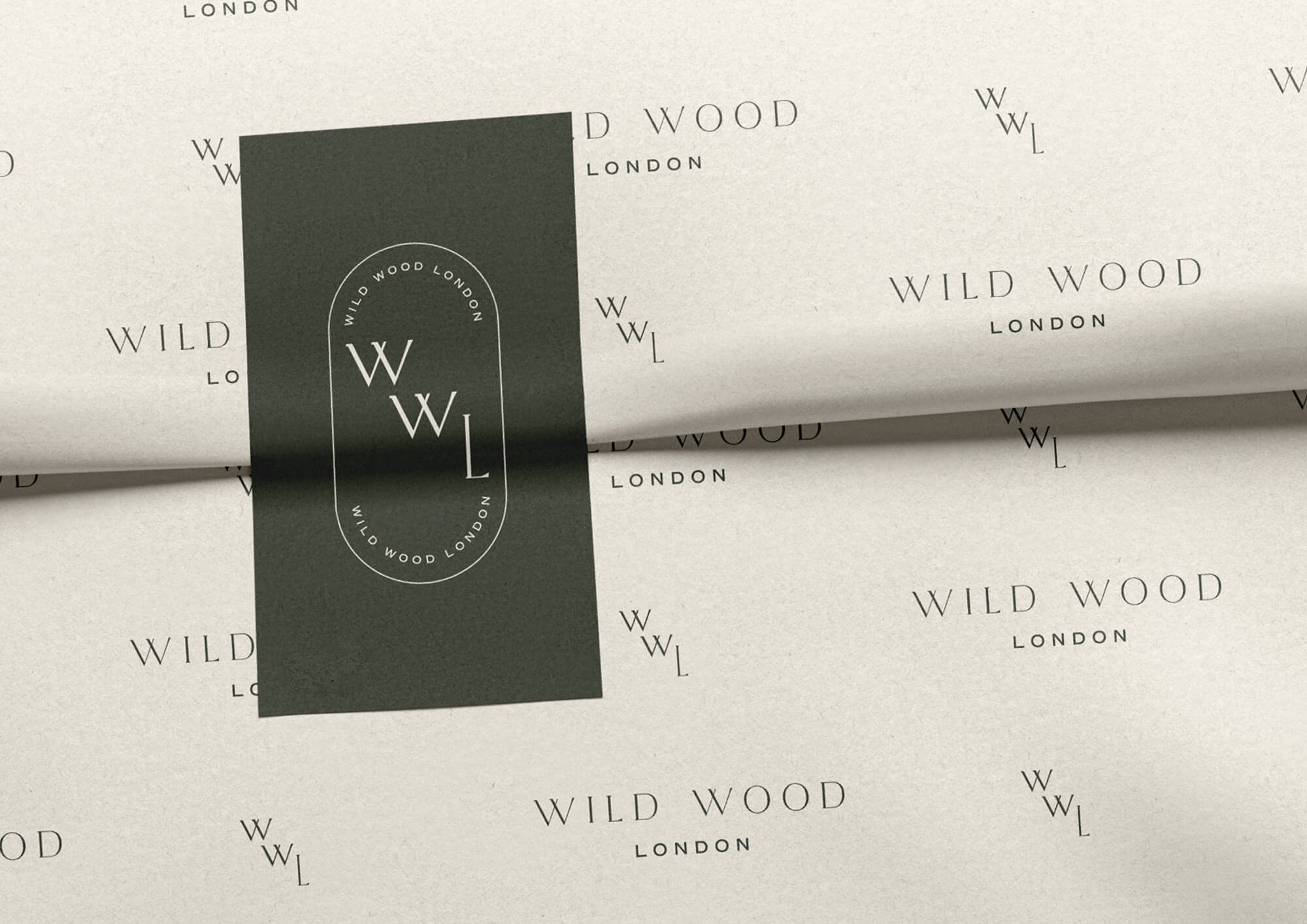 Close-up of white paper packaging with repeated black text 'WILD WOOD LONDON' and a black vertical label featuring the same text in a circle and a large 'WWL' in the center.