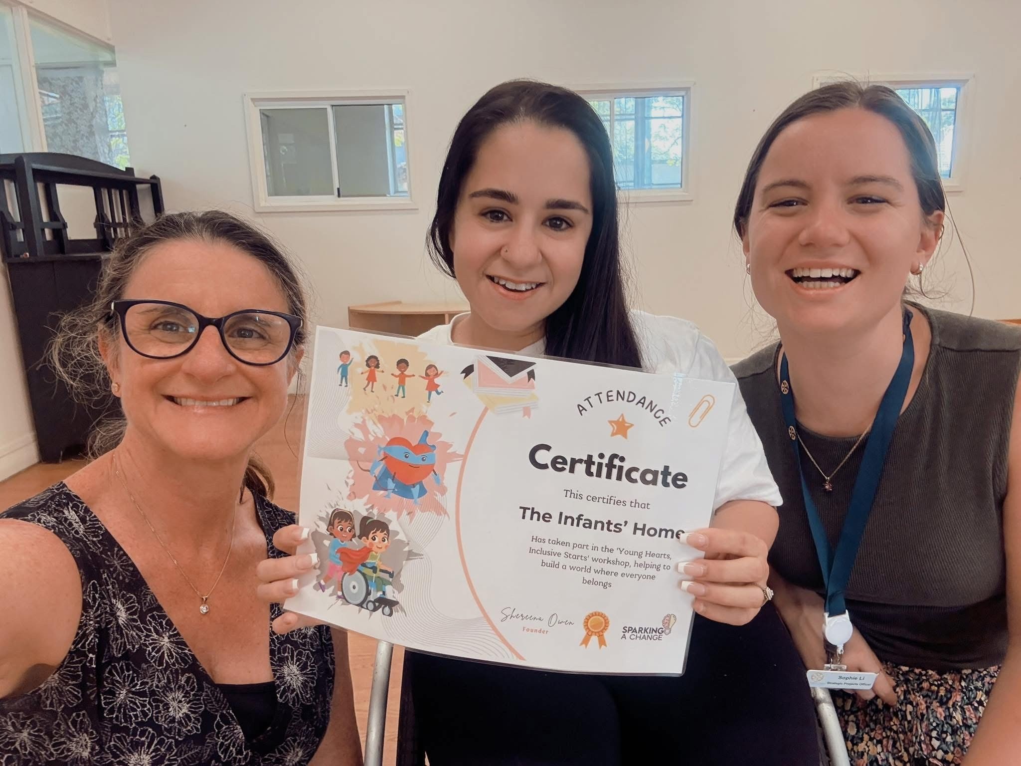 Three women smiling and holding a certificate at an indoor event.