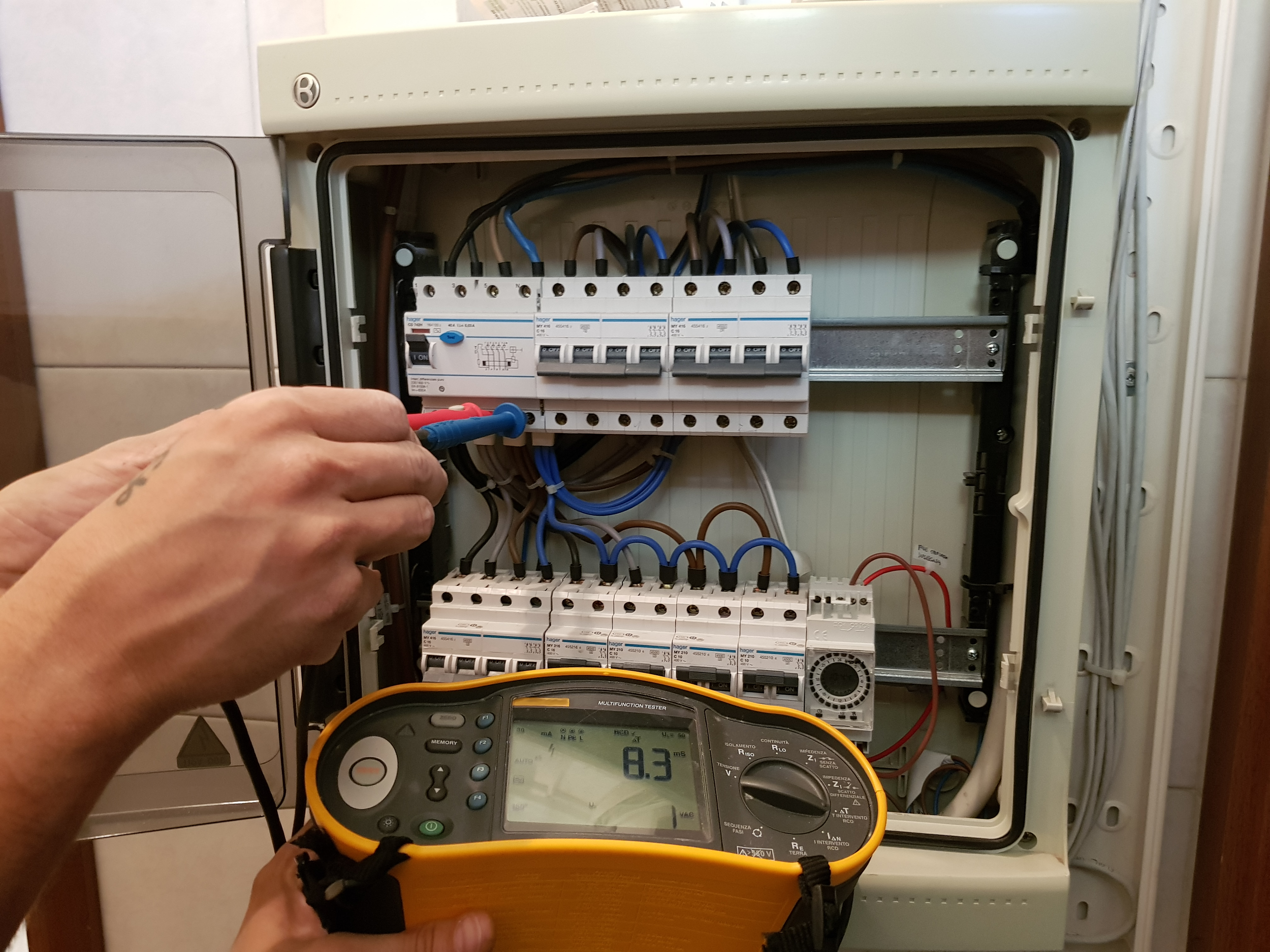 Un tecnico utilizza un multimetro digitale per misurare i valori elettrici di un quadro di distribuzione.
