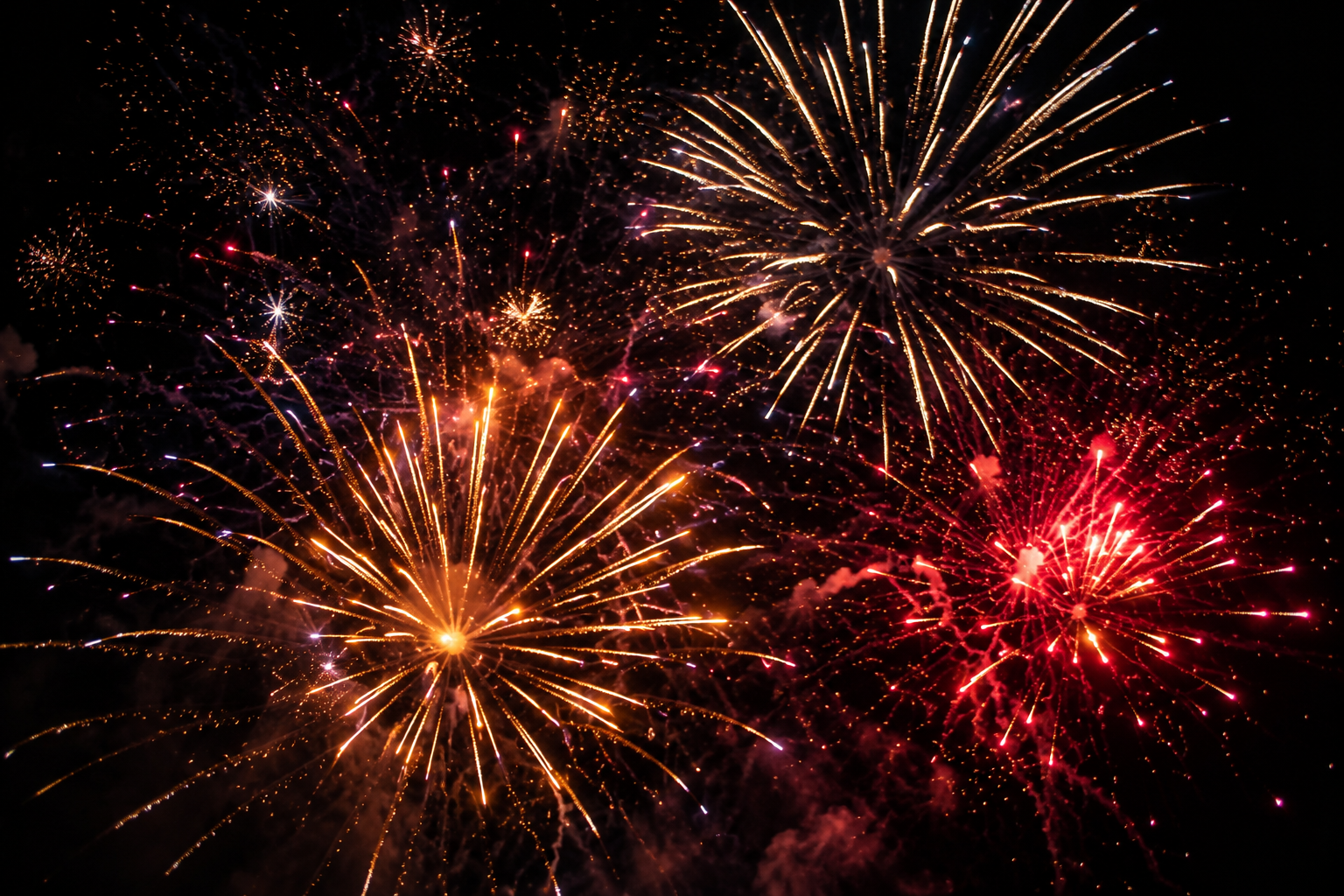 Fireworks display lighting up the night sky with colorful explosions of light in gold, red, and purple hues.