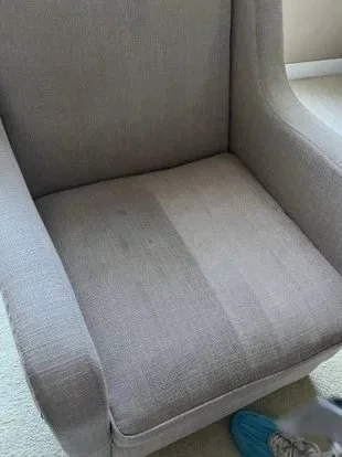 Close-up of a gray upholstered armchair with a wooden leg, located on a carpeted floor.