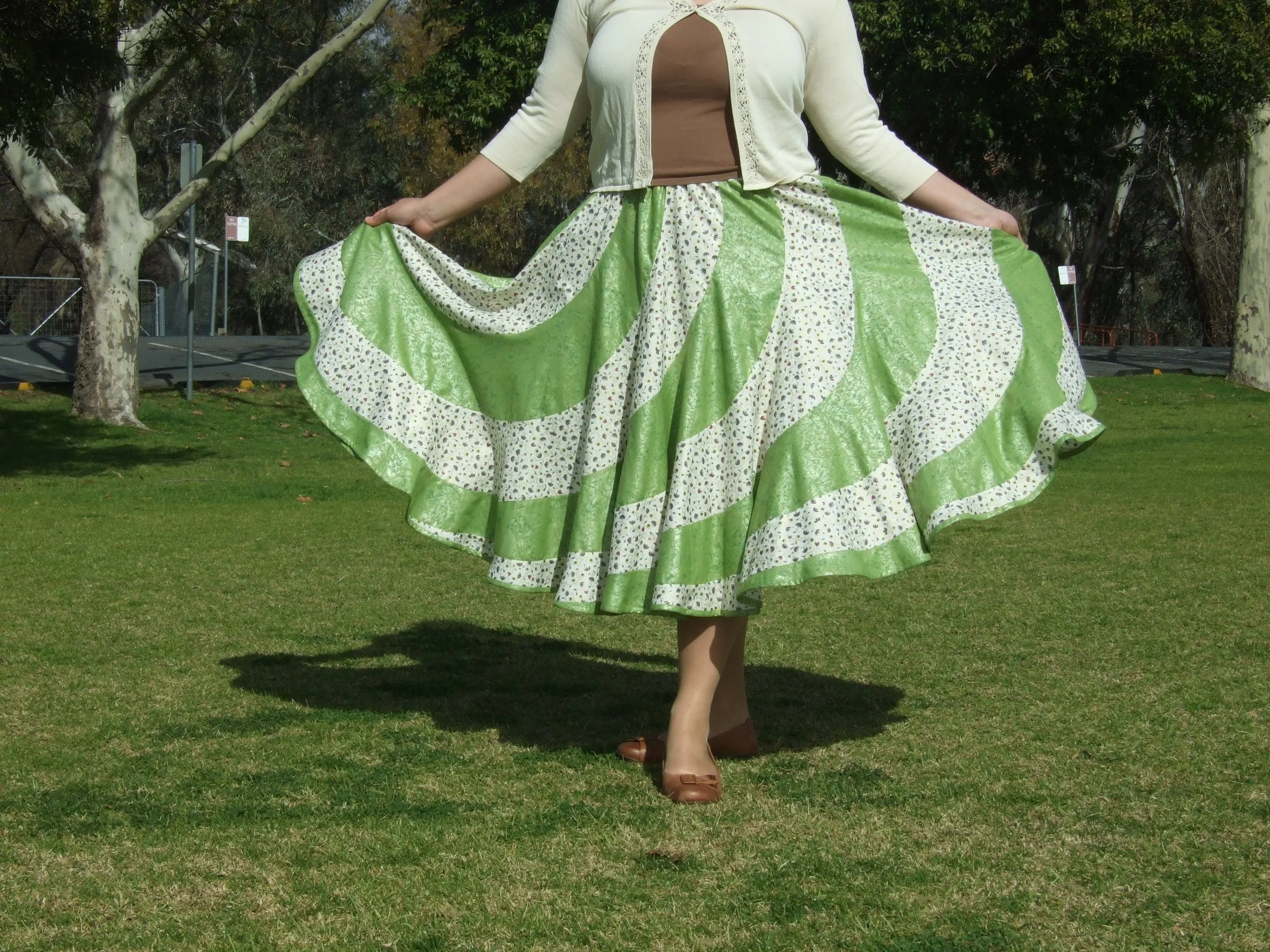 Woman wearing a Designs by Uriel Signature Swirl Skirt in olive and cream, with purple and turquoise floral details, olive swirling leaves and pearlised gold metallic accents.