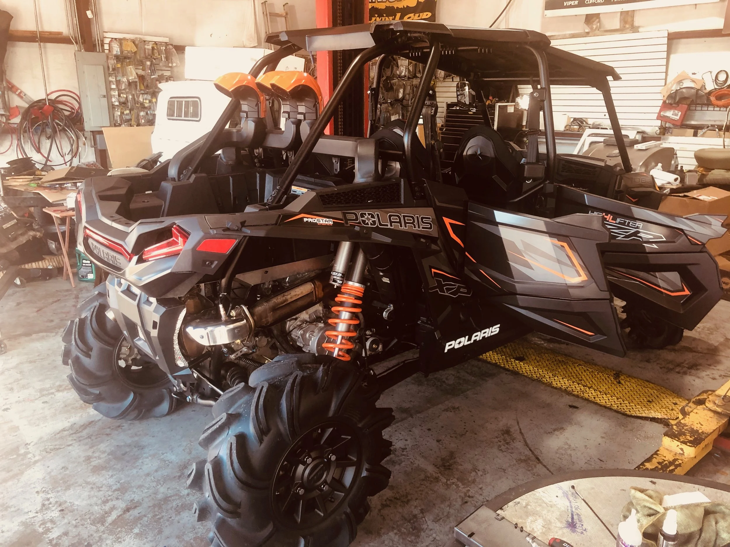 A Polaris off-road vehicle inside a workshop or garage with various tools, equipment, and storage items in the background.