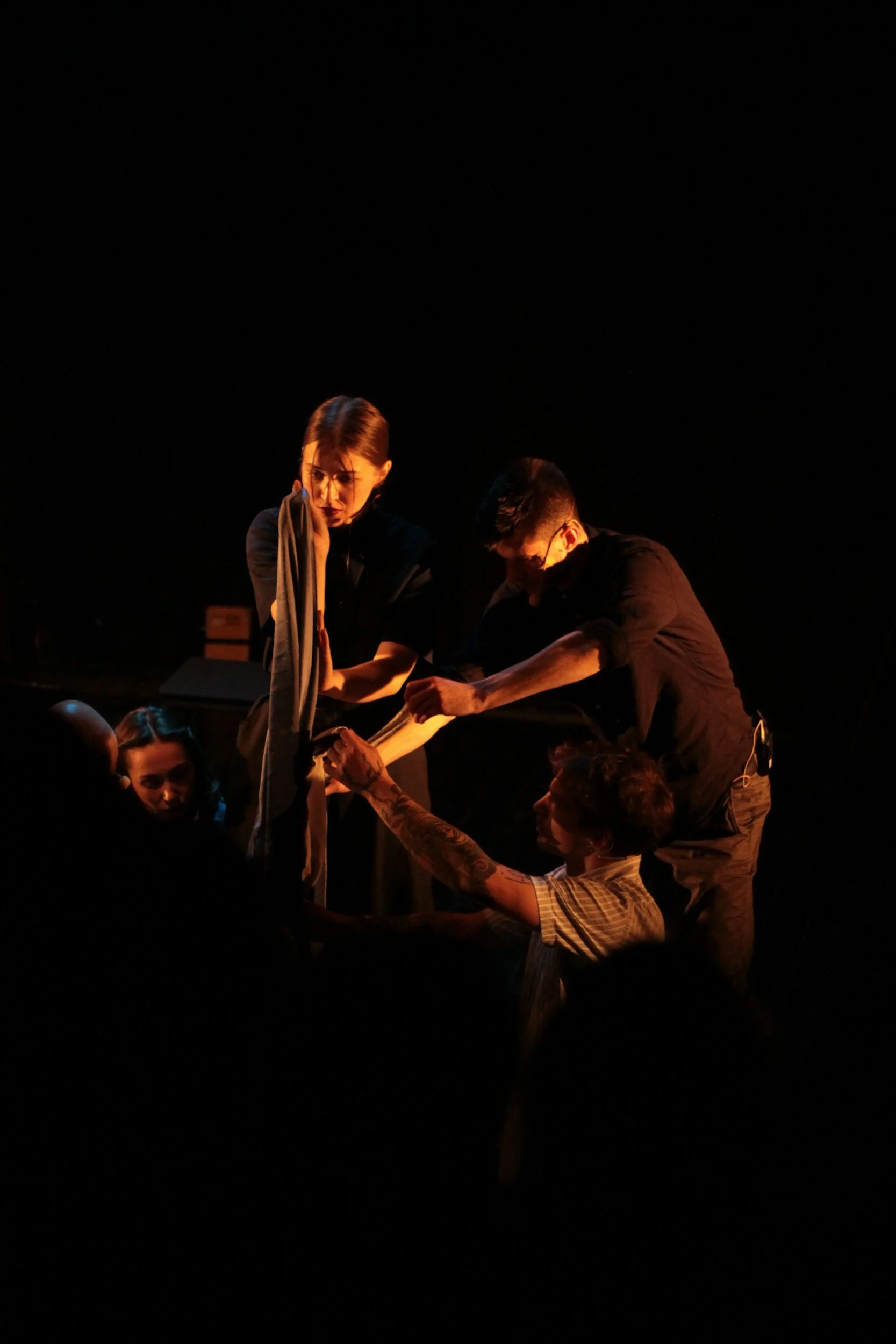 Two performers engaging in a scene on stage under warm stage lighting against a dark background, with a group of people watching.