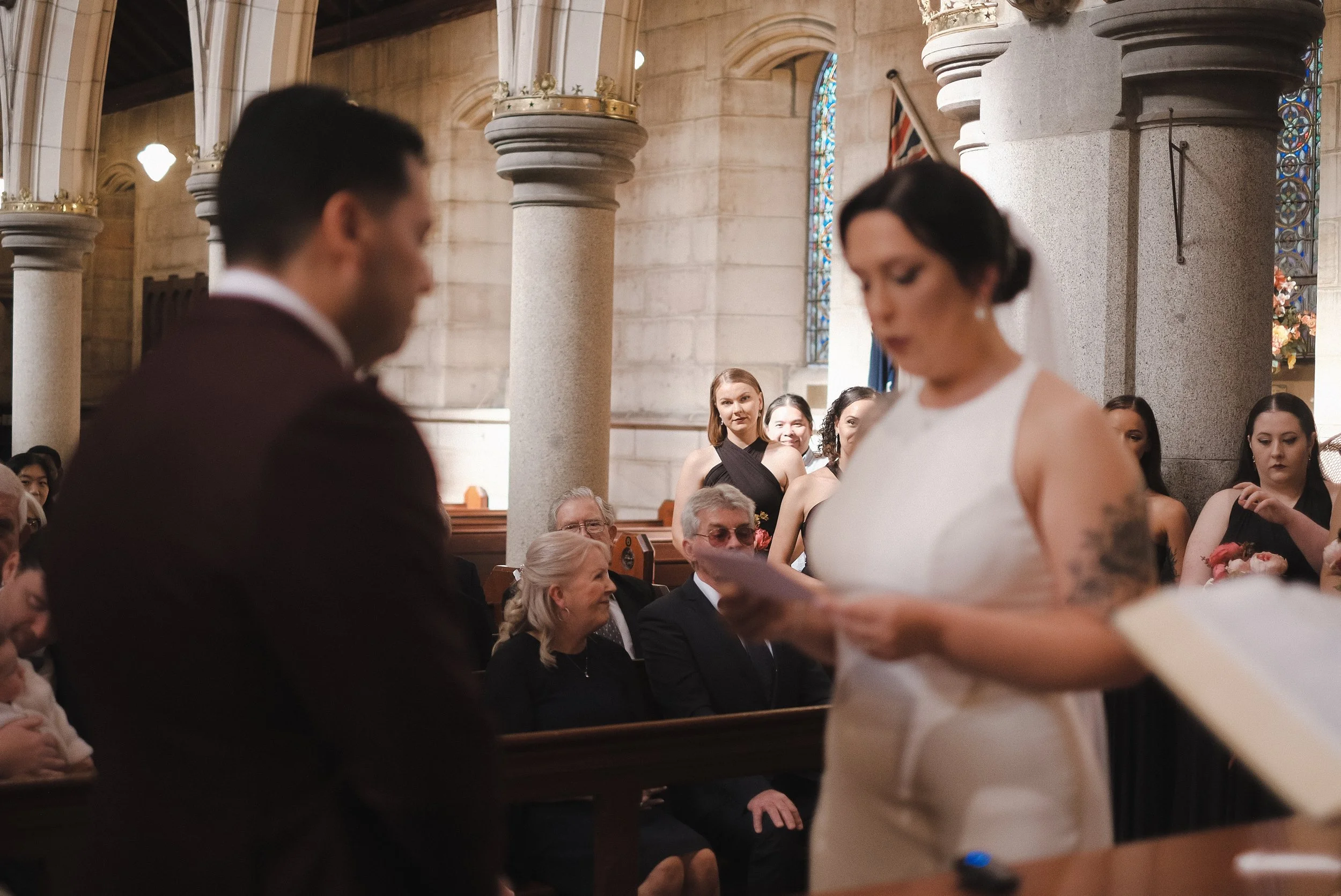 A wedding ceremony inside a church with a bride and groom at the altar, and guests seated in the pews watching.