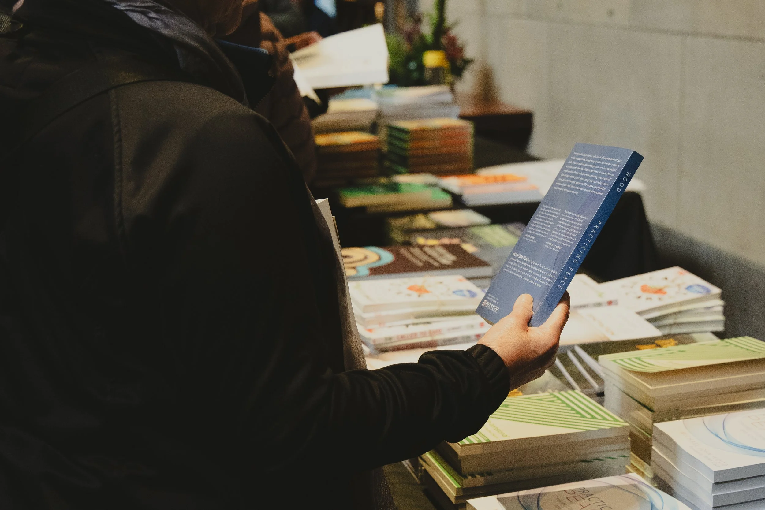 Person in dark jacket holding a blue brochure at a table displaying books and magazines.