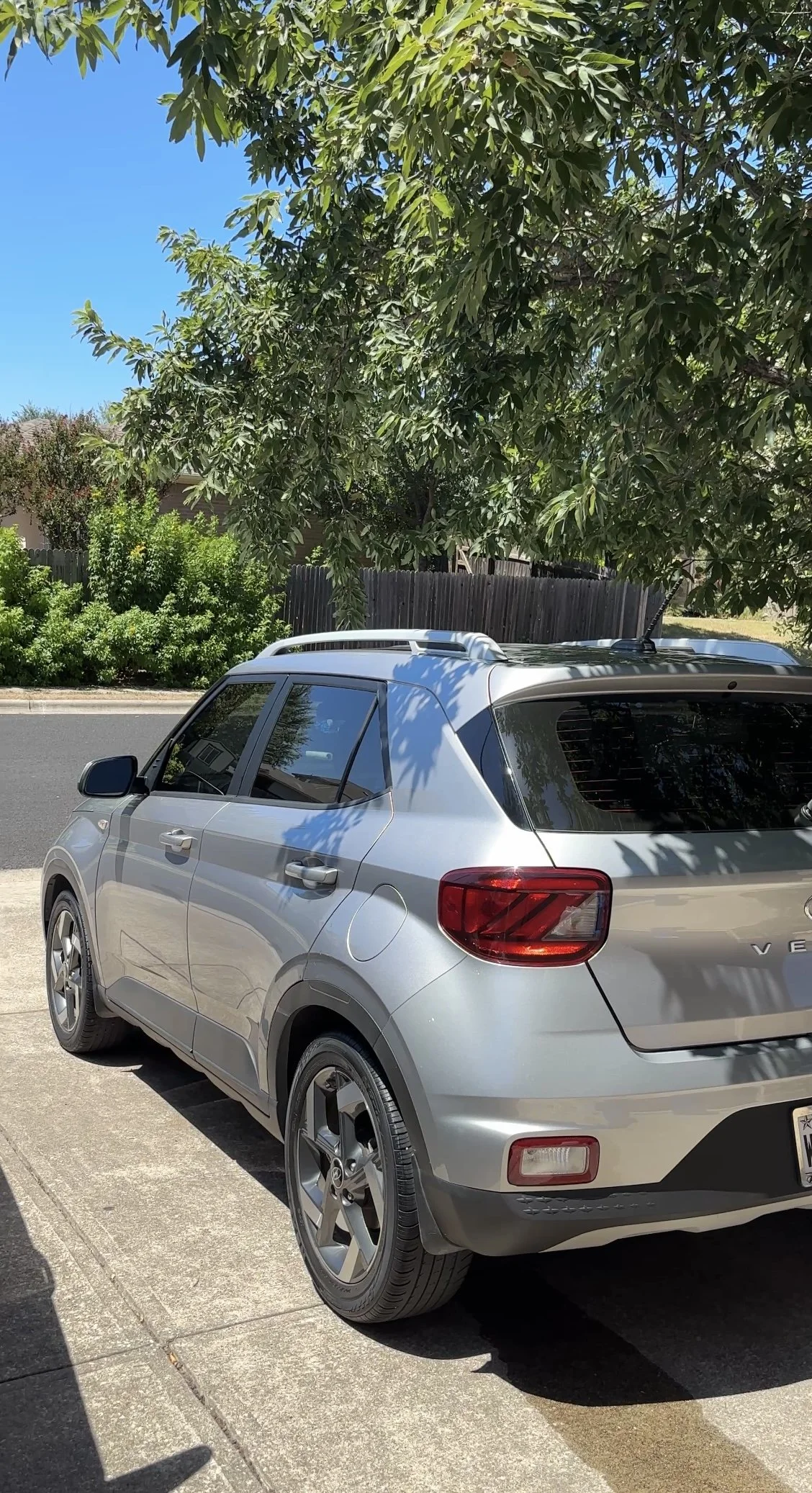 Silver Volkswagen SUV parked on a residential street near a sidewalk, with trees and a wooden fence in the background.