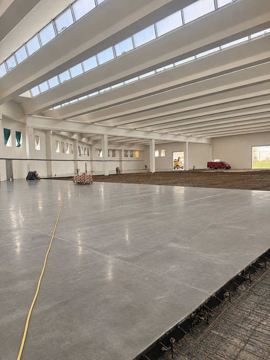 Interno di una grande struttura industriale in costruzione con pavimentazione in fase di completamento, ma ancora non finita.