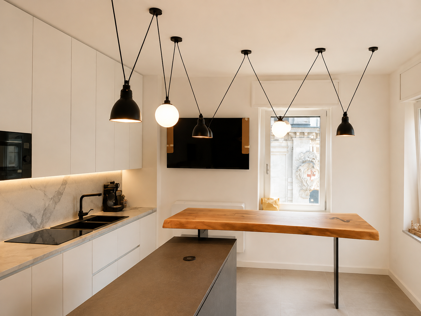 Cucina moderna con pensili bianchi, isola centrale con piano in pietra, lampade pendenti nere e bianche, televisore a parete, grande finestra con vista su un edificio storico.