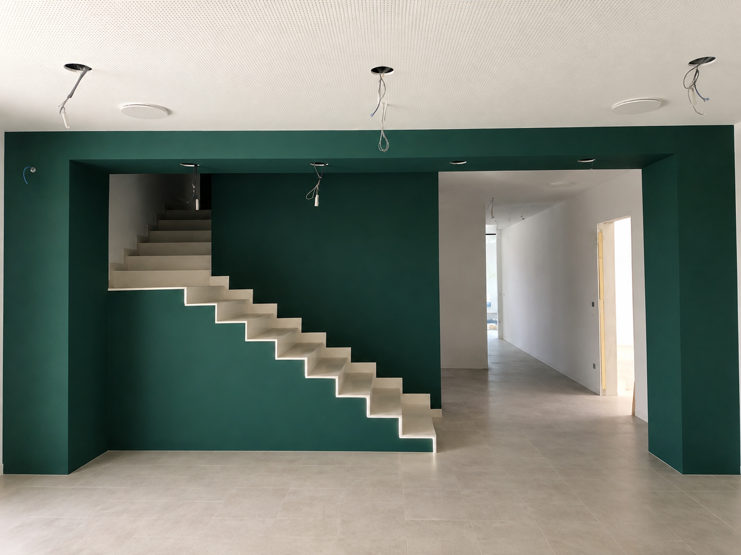 Interno di una casa in costruzione con pareti verdi e scala bianca, soffitto con punti luce non installati.