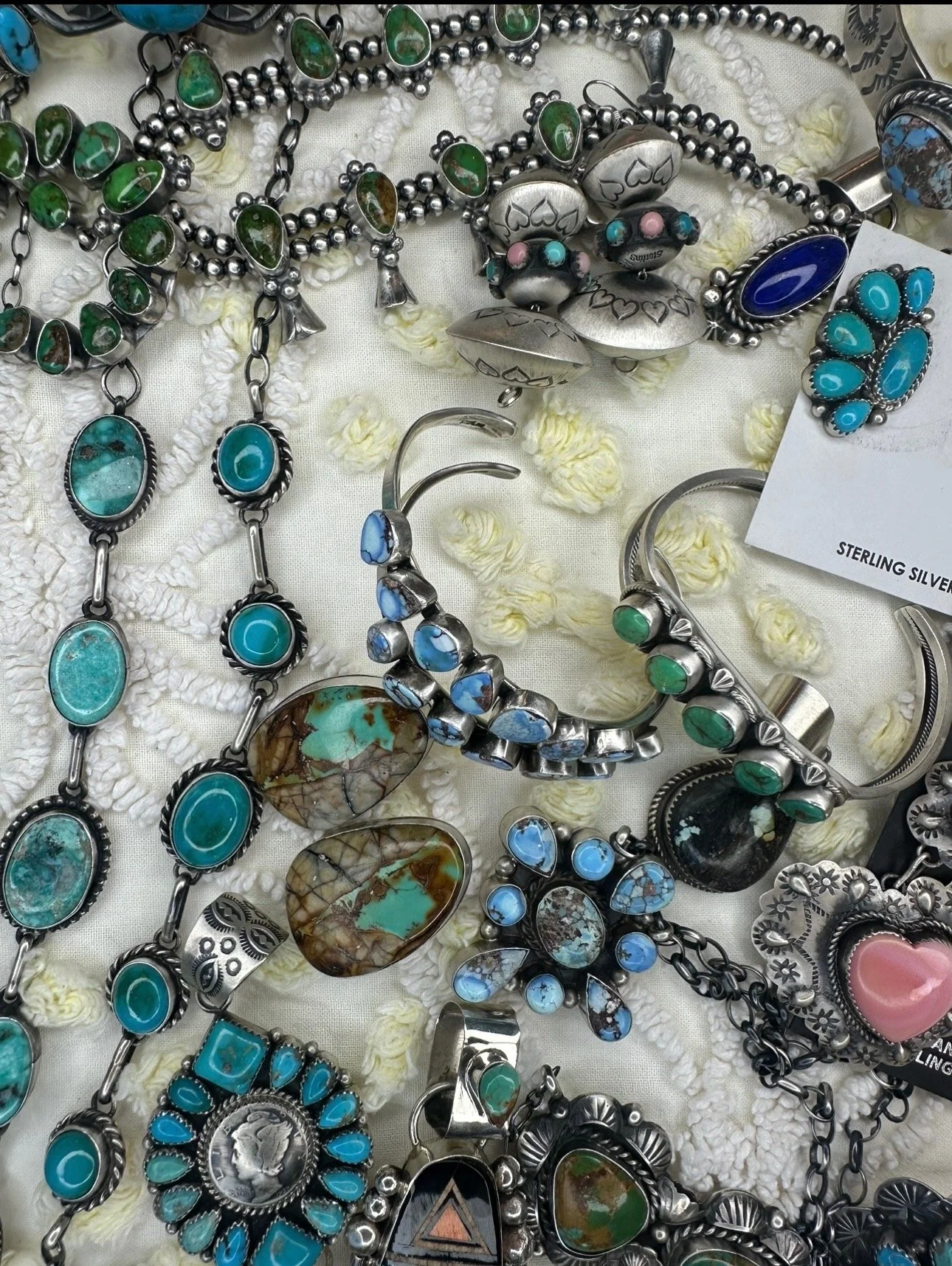 Assorted silver and turquoise jewelry including necklaces, bracelets, and rings on a white fabric background.