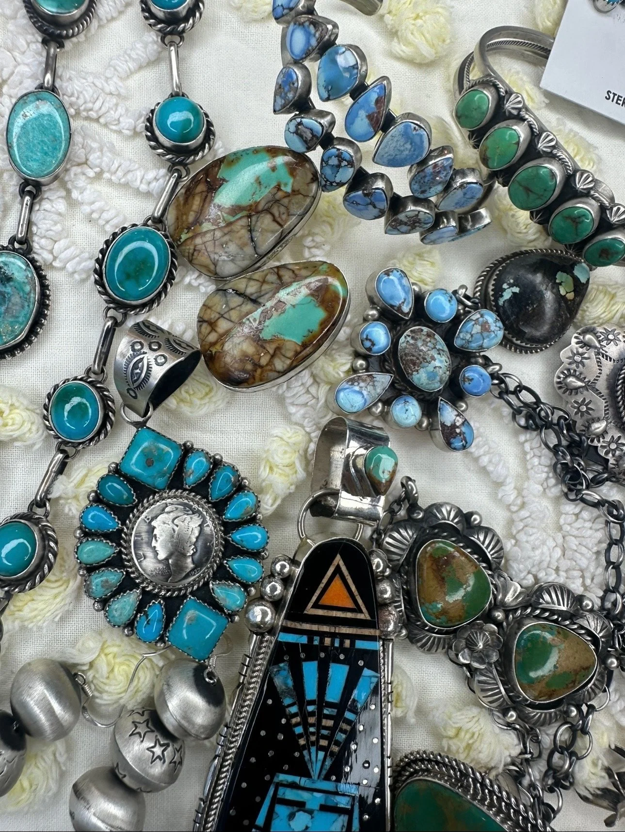 Collection of silver jewelry with turquoise and blue stones on a white textured surface.