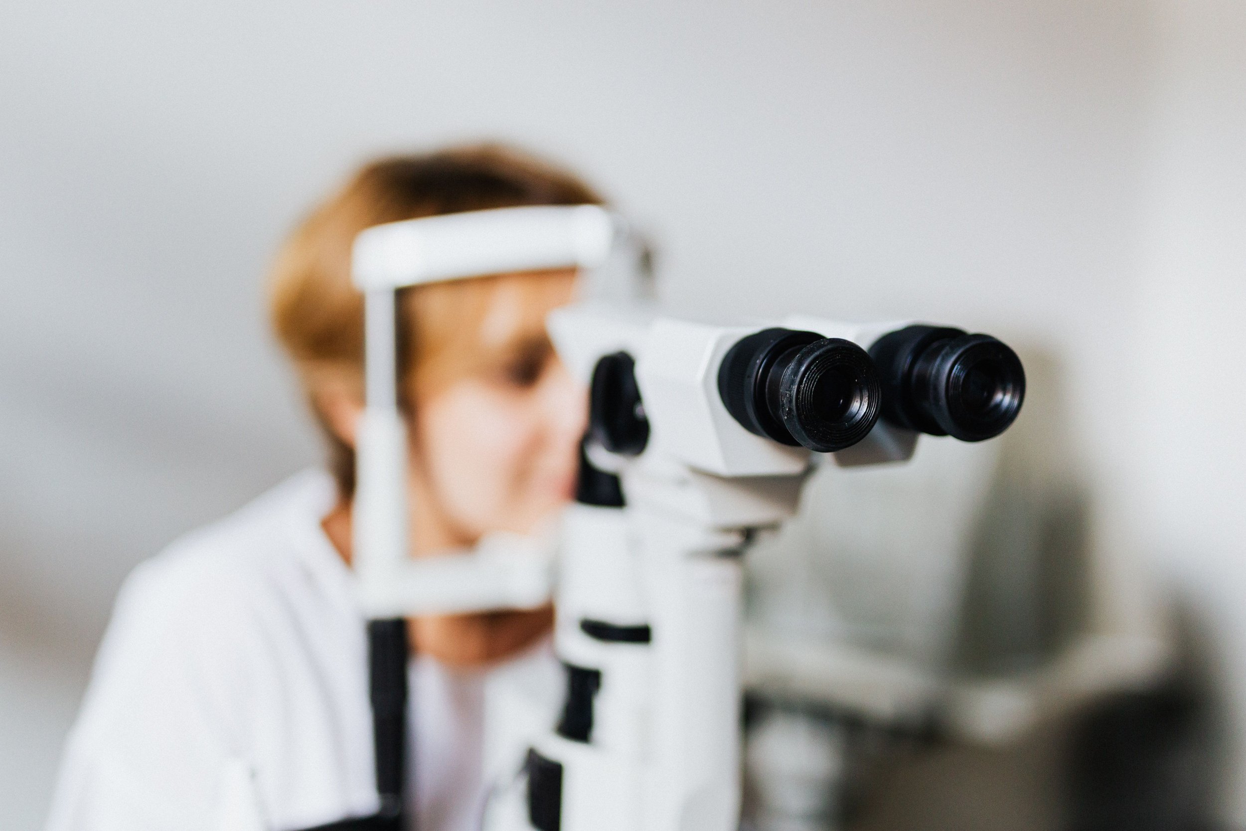 Person using a microscope to observe something, with their face partially visible in the background.