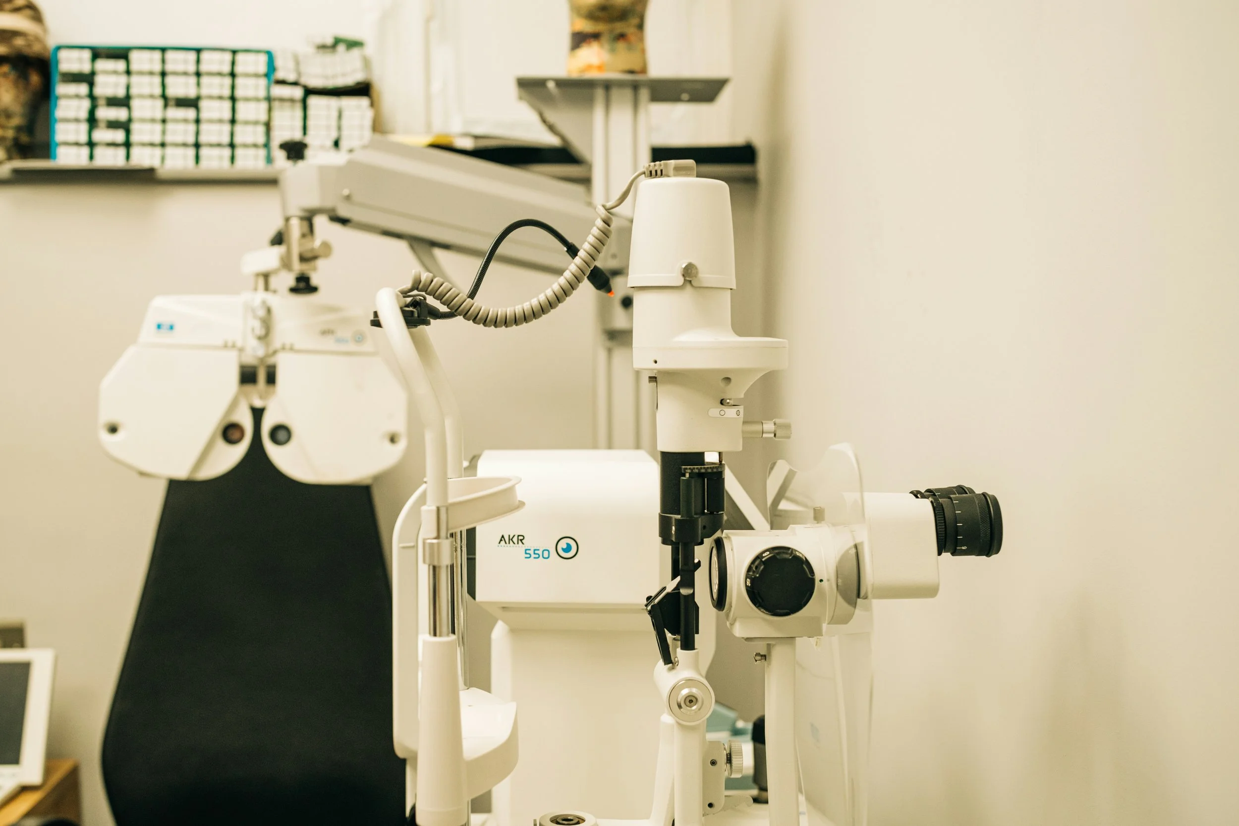 A scientific microscope setup in a laboratory with focus on the microscope's objective lenses and eyepiece, with shelves containing supplies in the background.