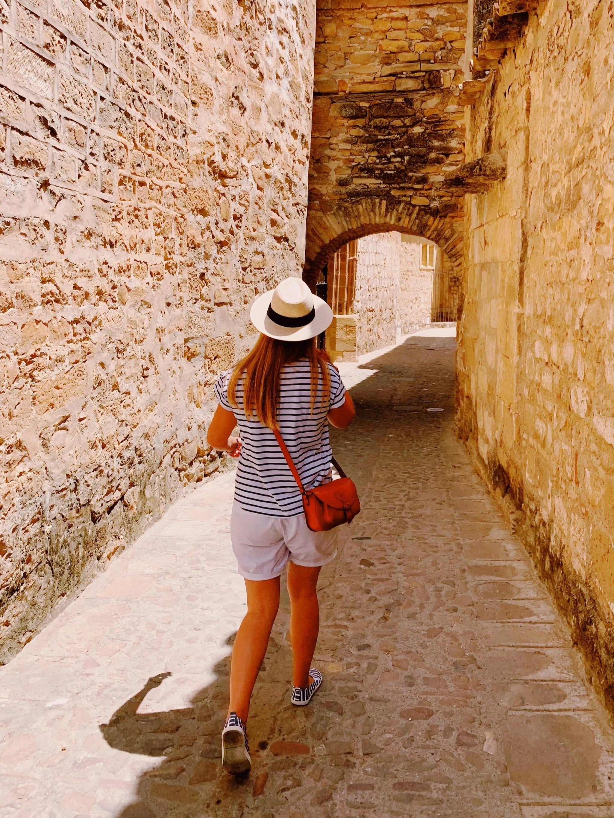 Woman in a wide-brimmed hat and striped shirt, walking through a narrow stone-walled market street in Israel, on a Holyland Horizons tailor-made private tour
