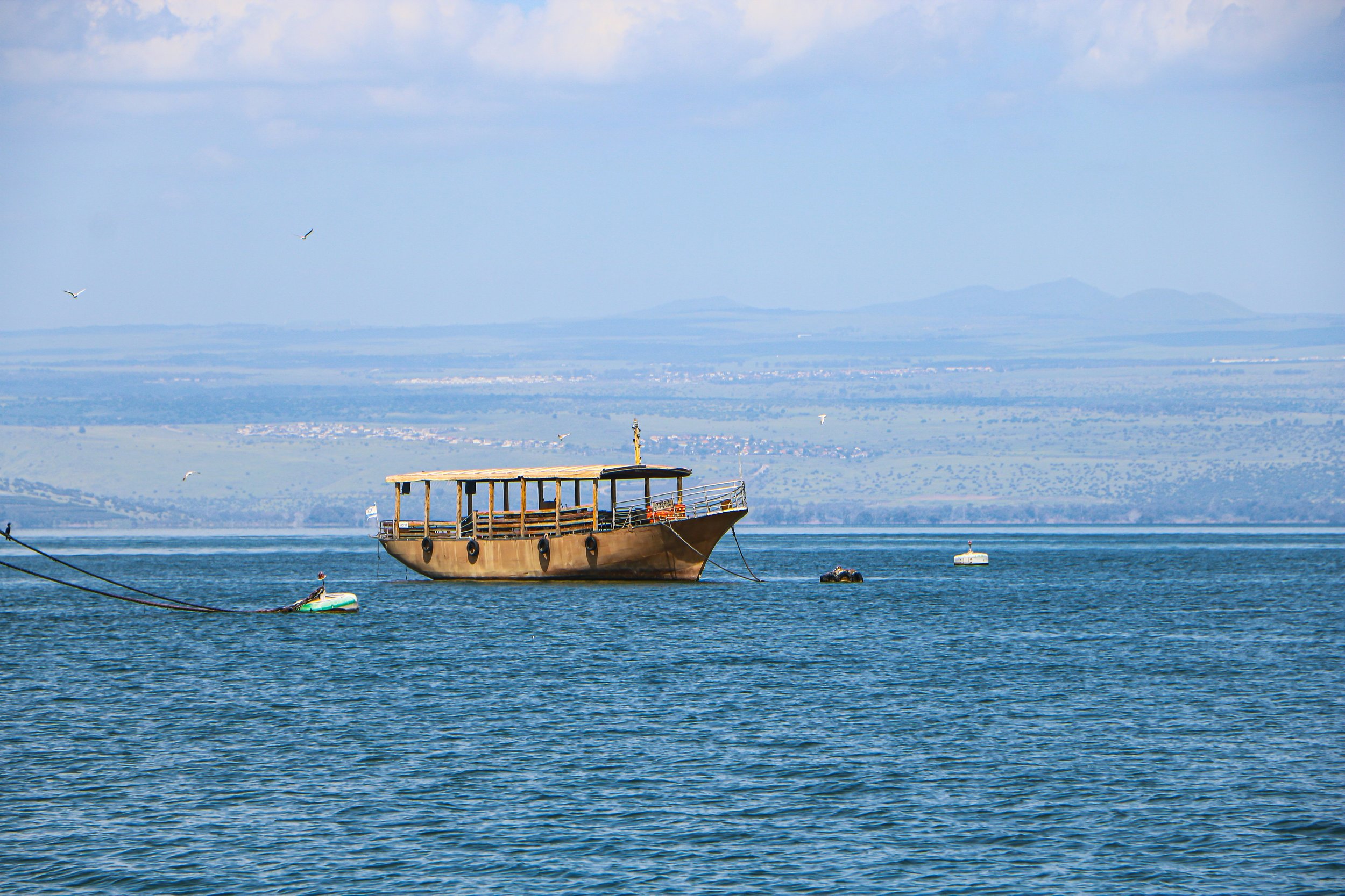Wooden boat sailing on the Sea of Galilee, Israel, with mountains visible in the background — a highlight of Holy Land pilgrimage journeys with Holyland Horizons